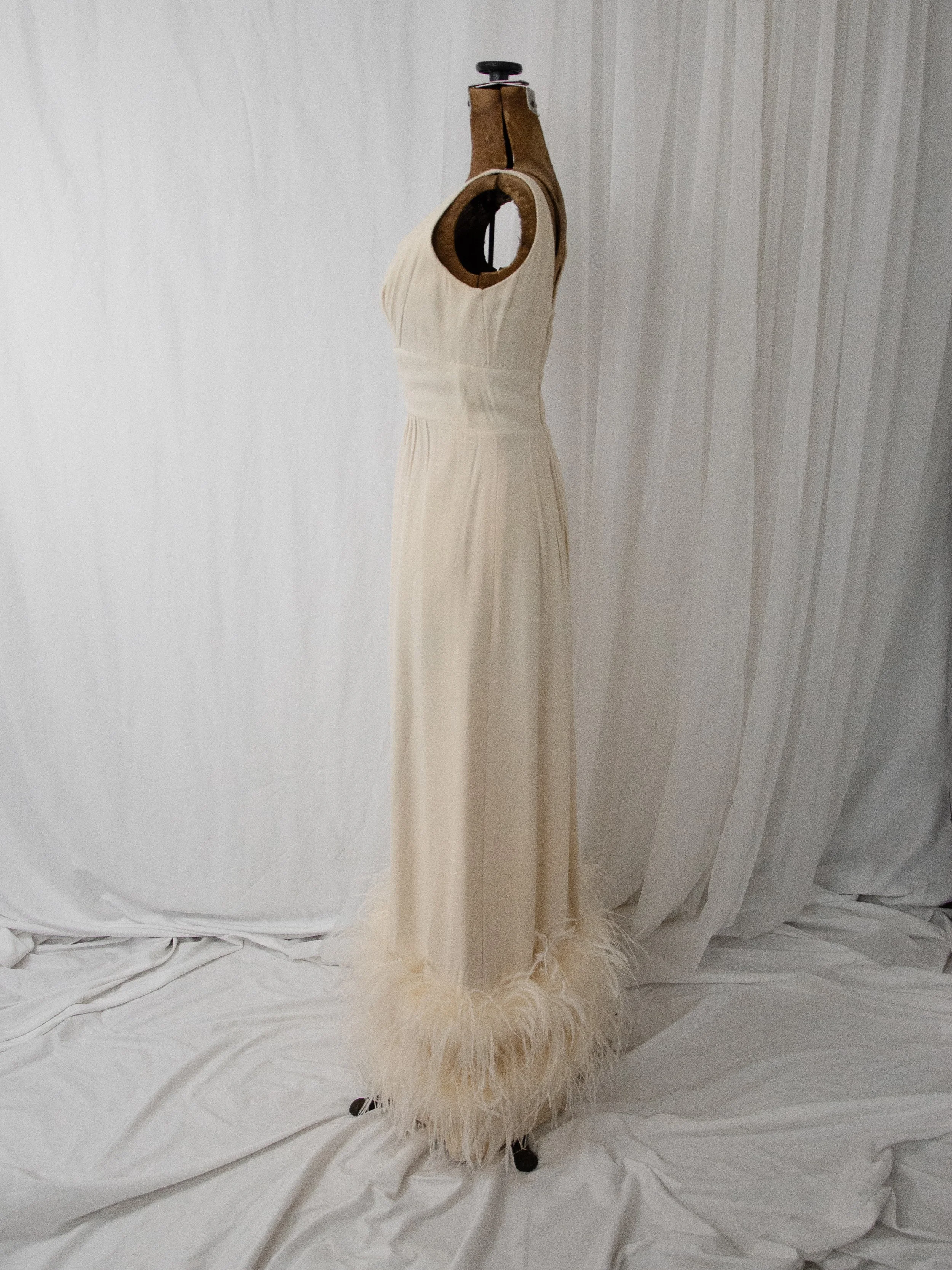 Side view of the late 1950s cream crepe gown on a dress form, showing the sleeveless bodice and feather hem.