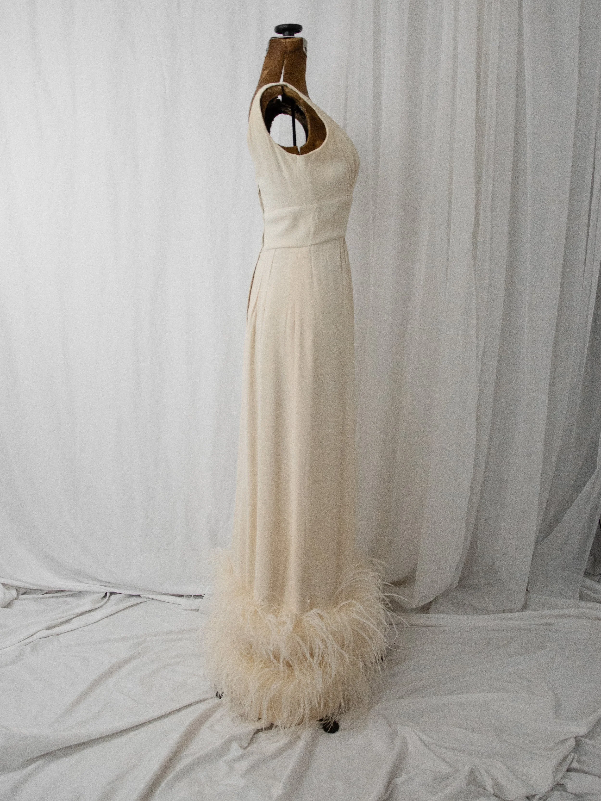 Opposite side view of the late 1950s cream ostrich feather gown on a dress form.