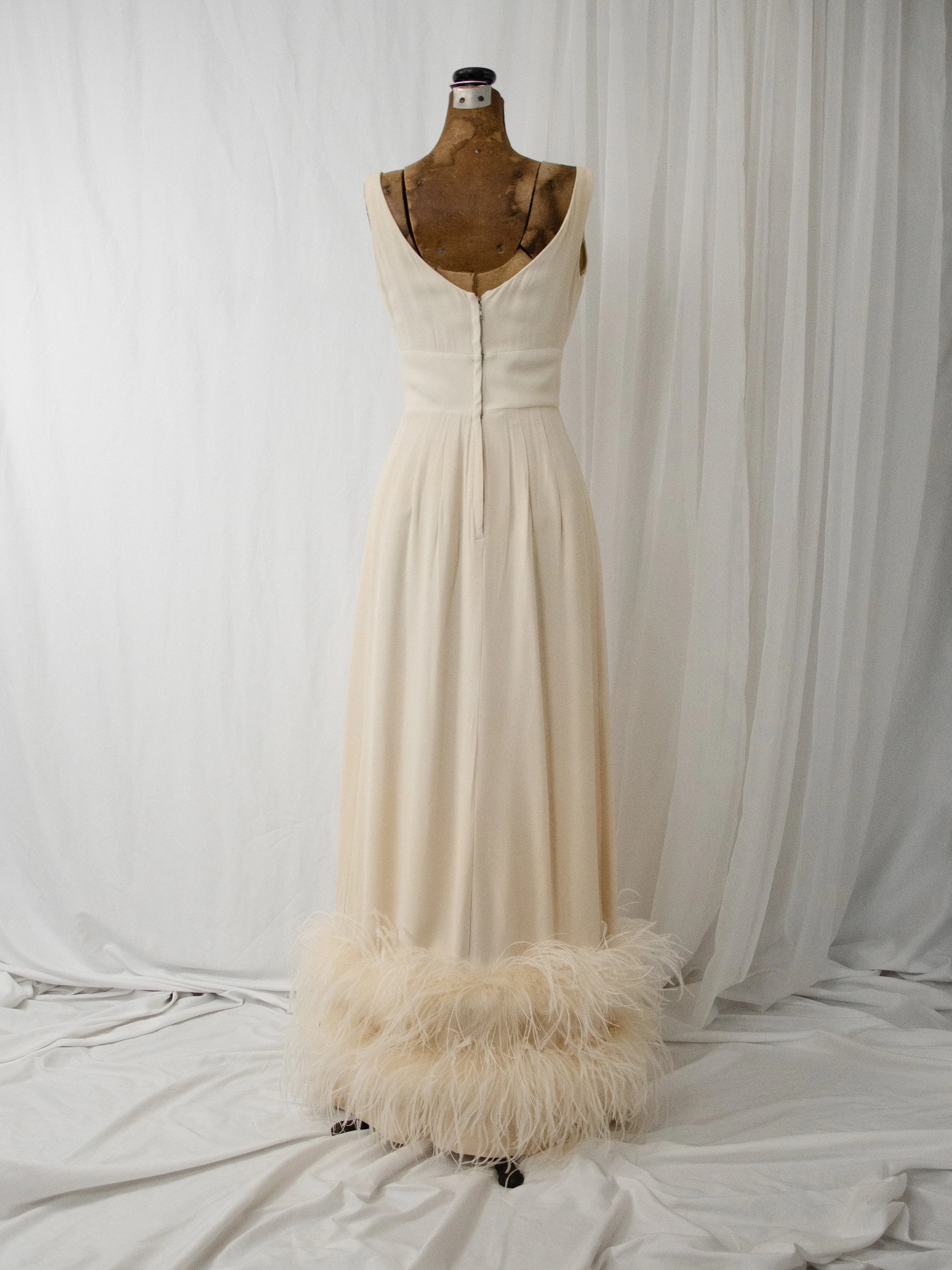 Back view of the late 1950s cream crepe gown on a dress form, showing the scooped back and feather hem.