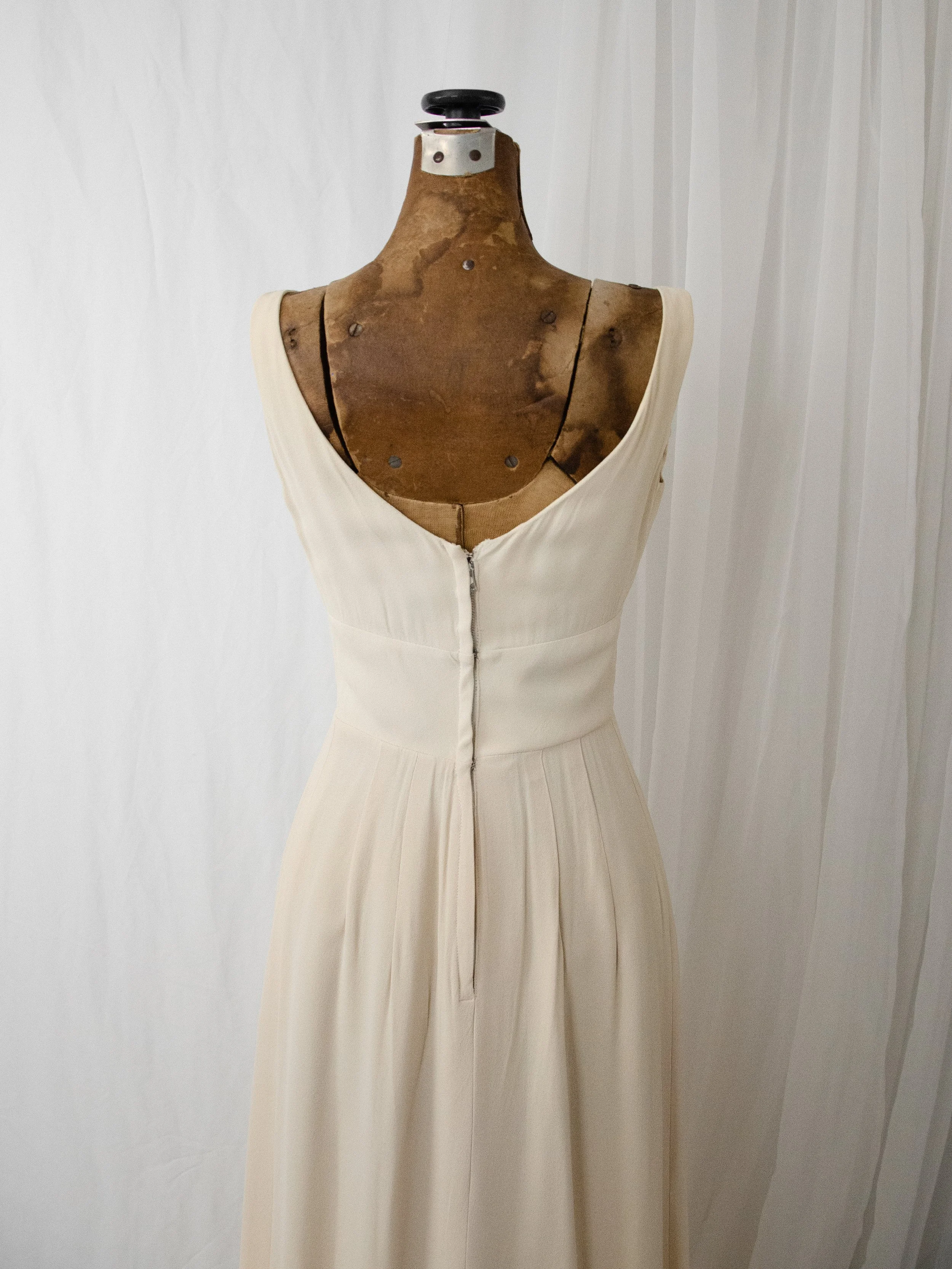 Close-up of the late 1950s cream gown's back bodice on a dress form, showing the scoop back and closure.