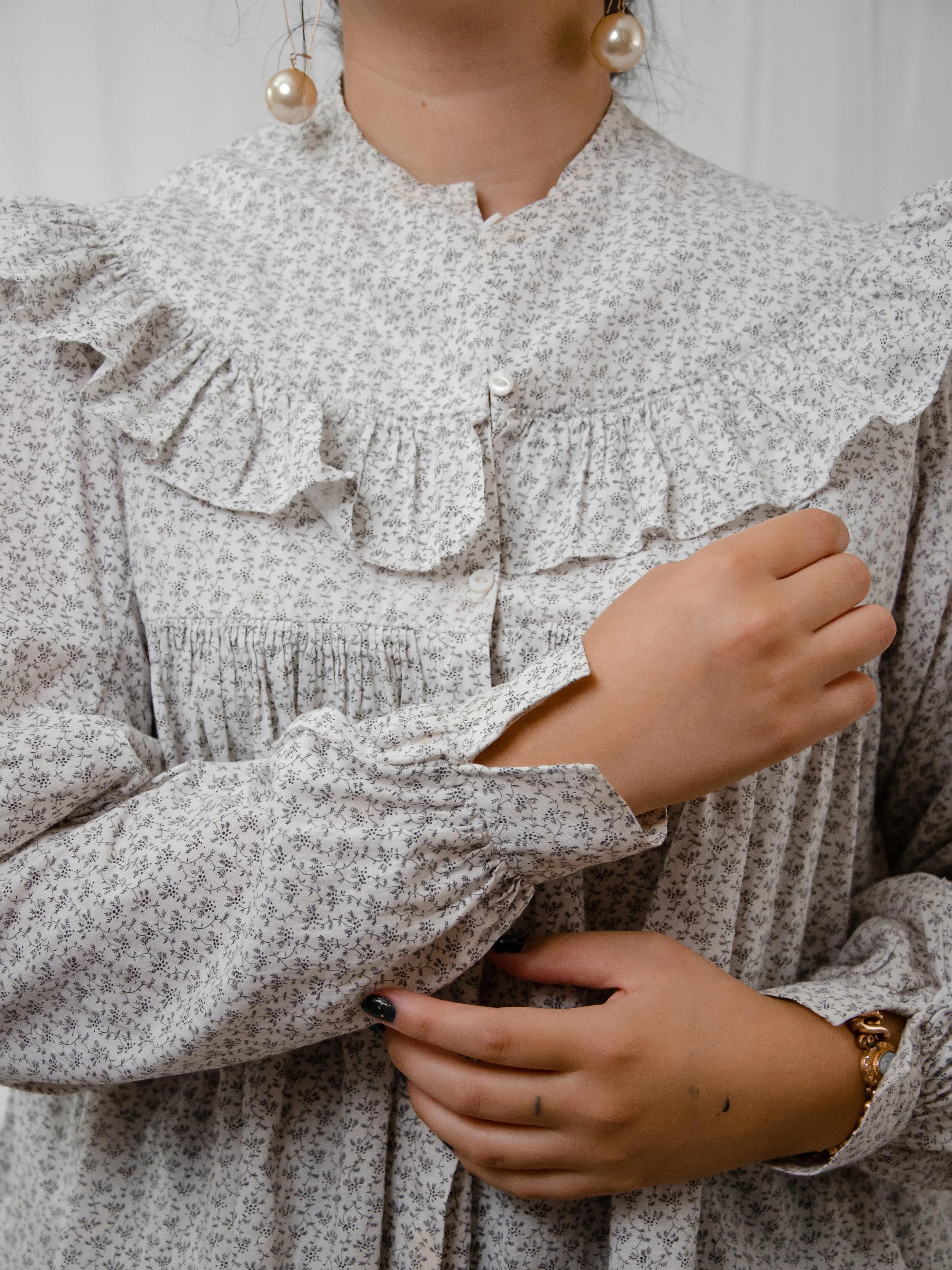 Close-up of the Victorian calico top on a model buttoning the cuff, showing the ruffle collar.