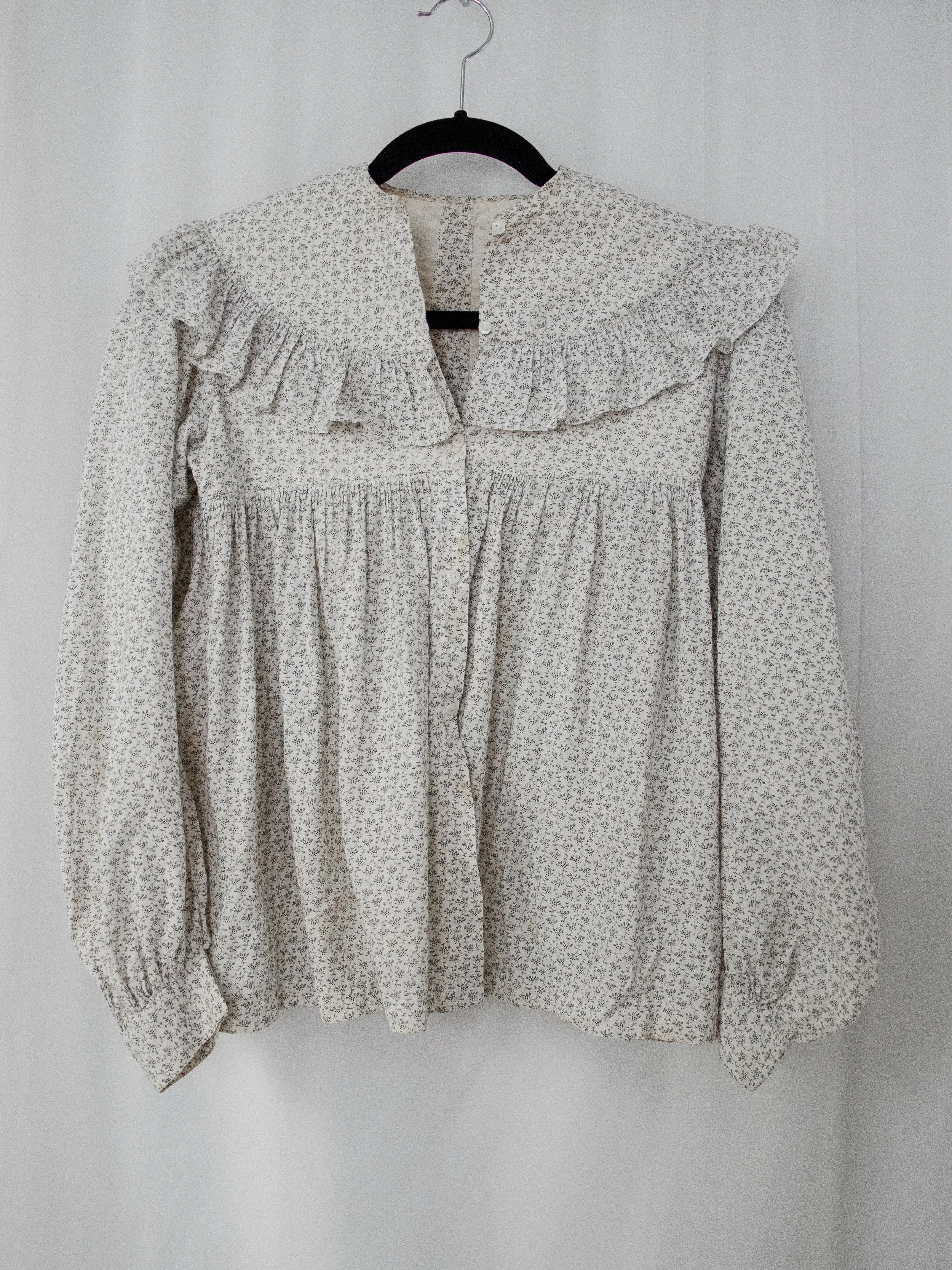 1890s Victorian floral calico prairie top on a hanger, full front view with ruffle yoke and long sleeves.