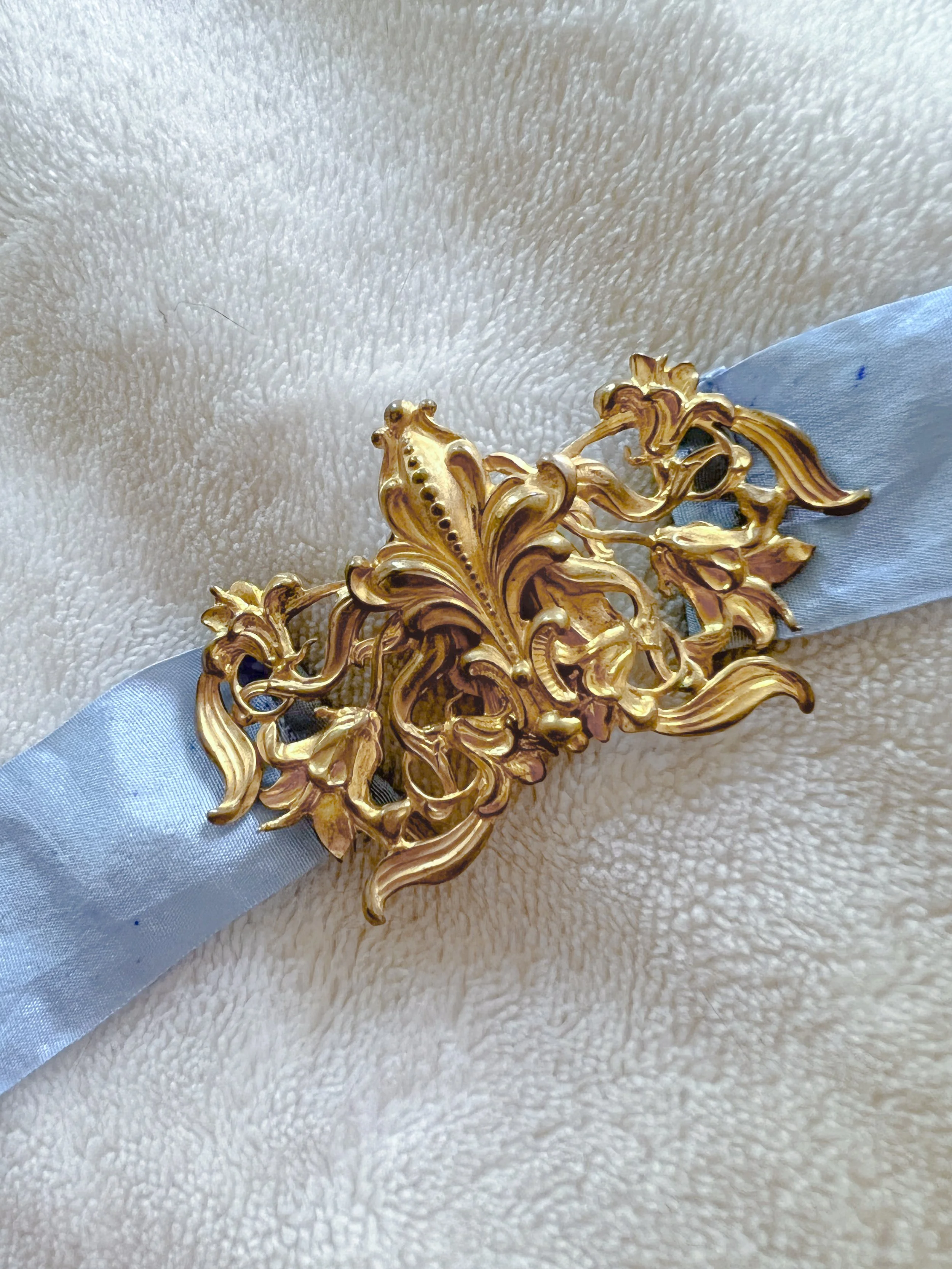 Close-up of the 1930s gold metal filigree art nouveau buckle on a sky blue silk ribbon belt.
