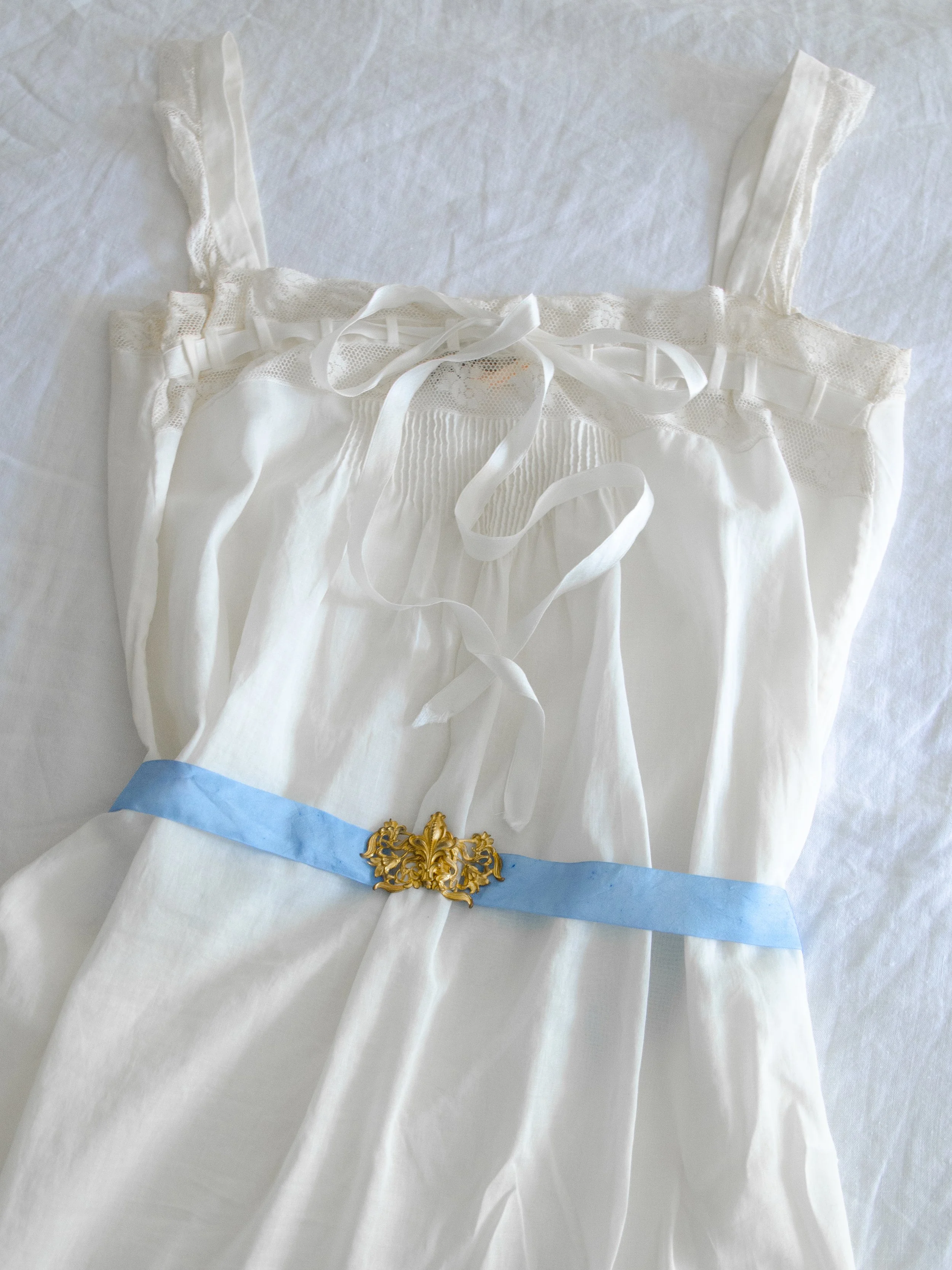 1930s sky blue silk ribbon belt with gold filigree buckle, styled around a white cotton slip laid flat.