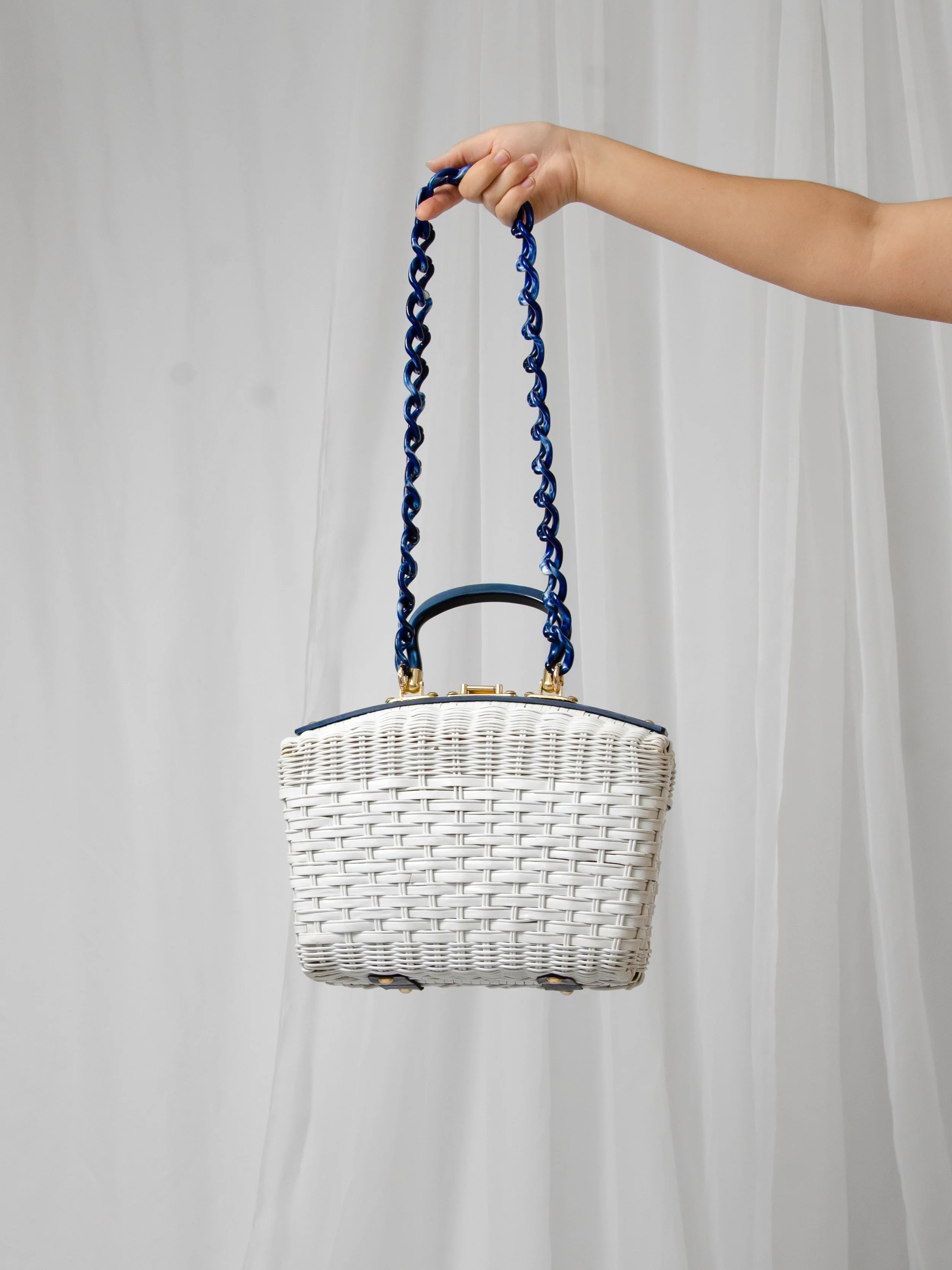 Back view of the 1950s white wicker handbag hanging from its blue marbled chain strap.