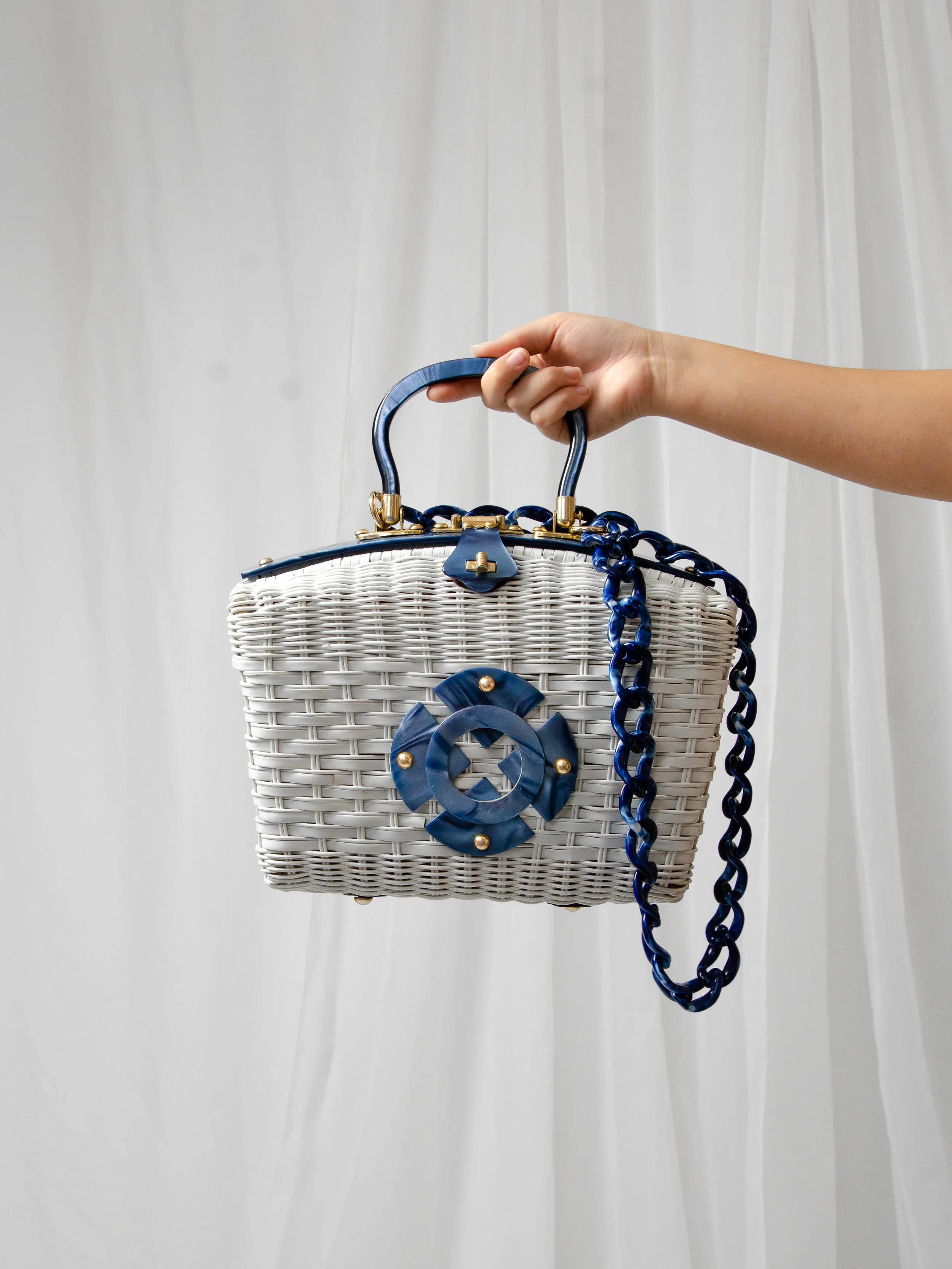 1950s white wicker and blue lucite purse held by its curved top handle, chain strap draped down.