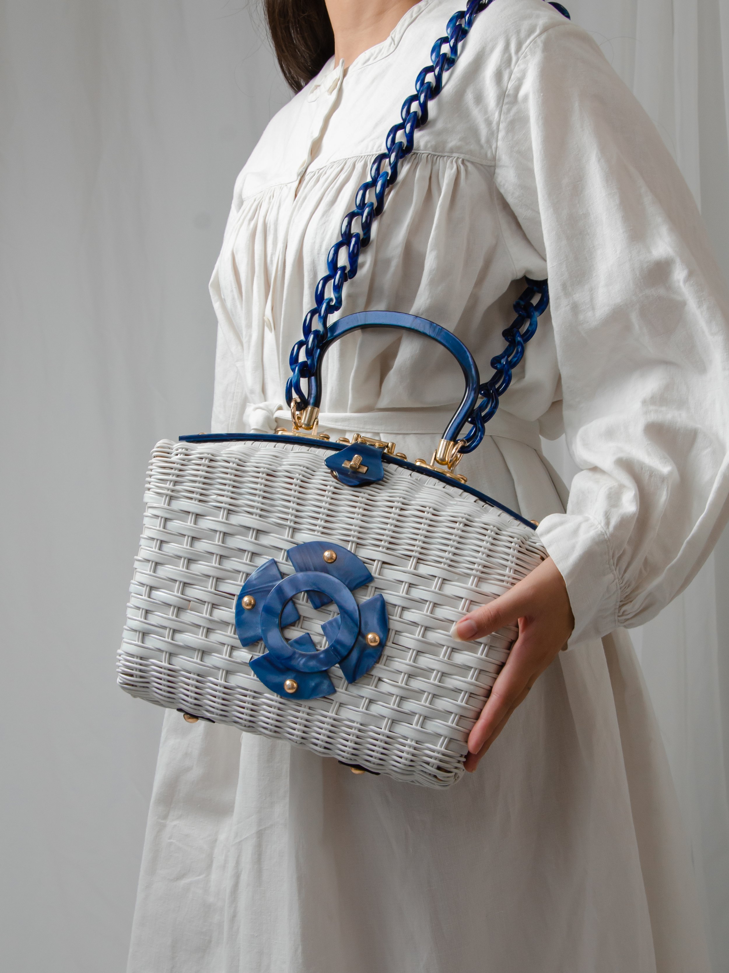 1950s white wicker handbag with marbled blue lucite medallion and chain strap, worn on a model's shoulder.