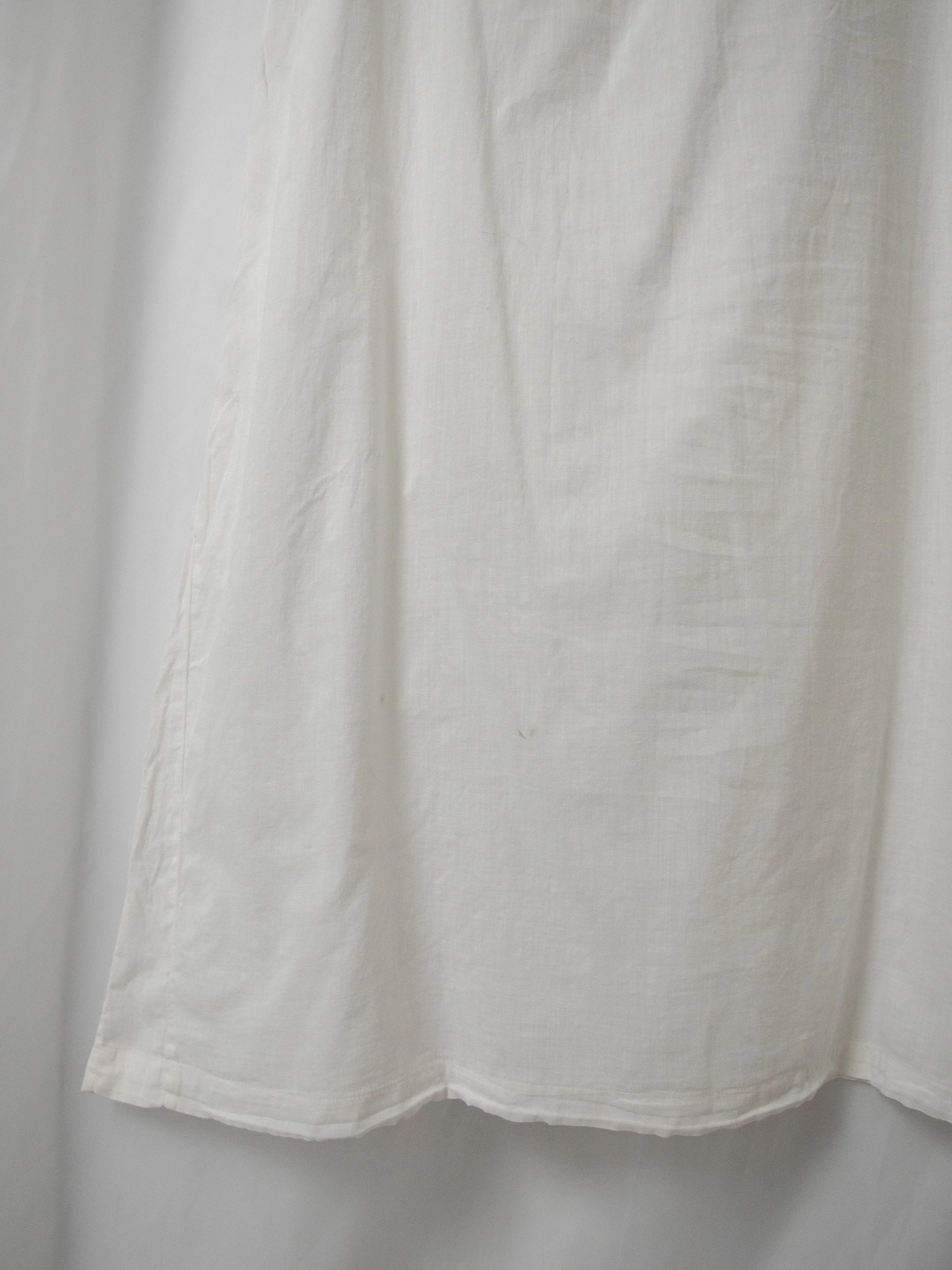 Detail of the antique white cotton off-shoulder dress skirt, showing the plain cotton hem.