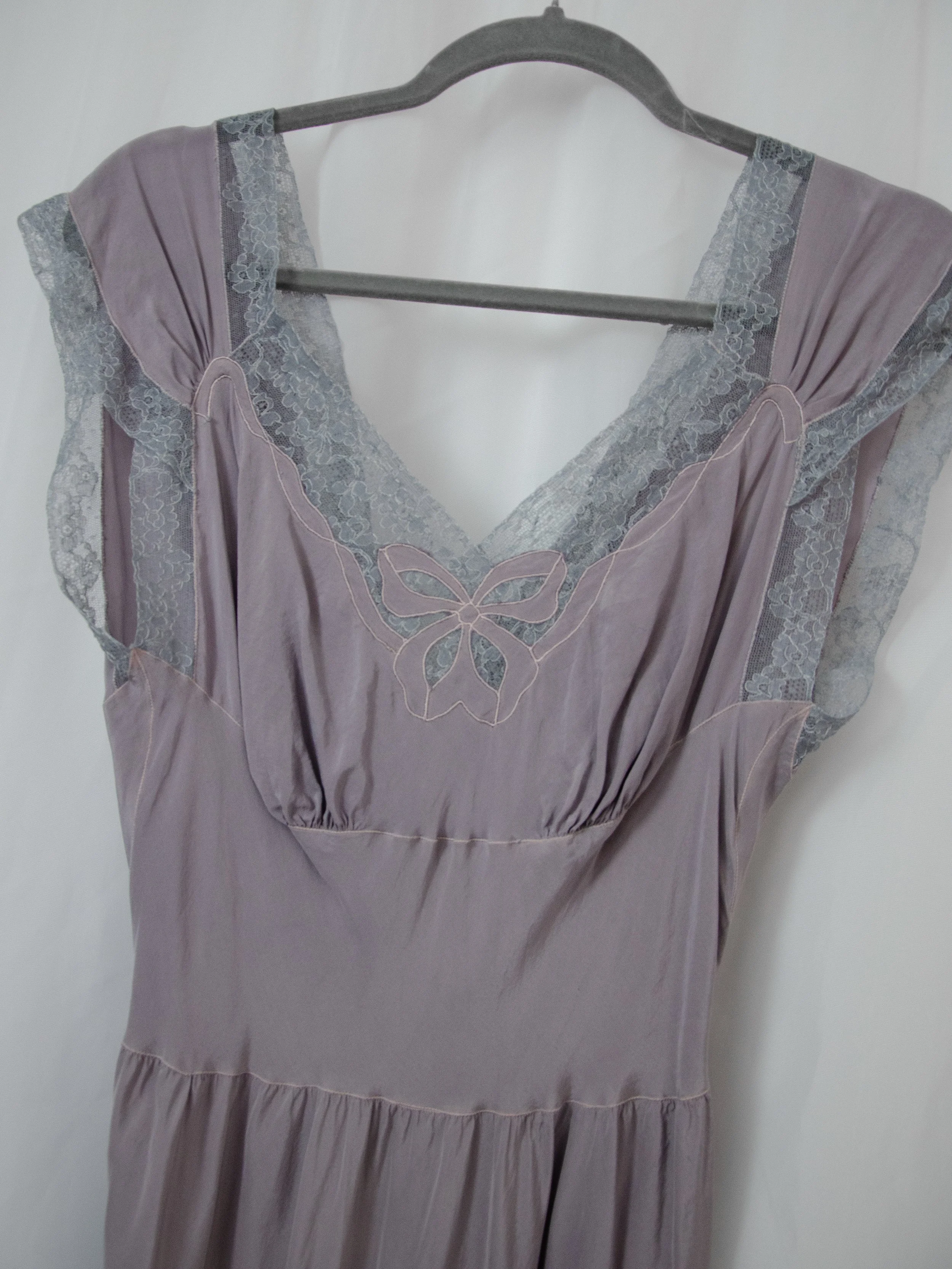 Close-up of the 1940s lavender silk dress bodice on a hanger, showing lace cap sleeves and bow appliqué.