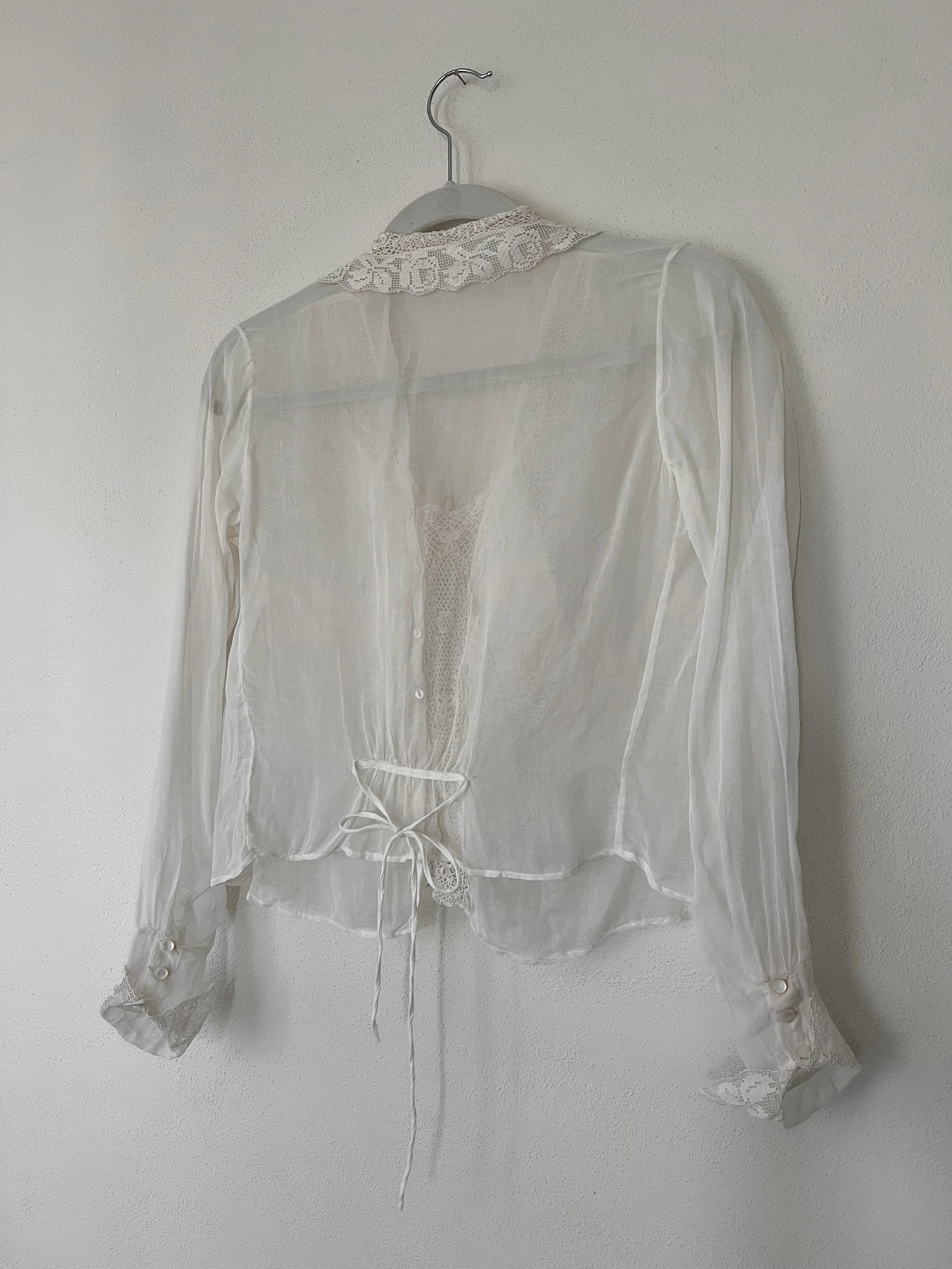 Back view of the late Edwardian sheer white blouse on a hanger, showing the lace collar and back waist ties.