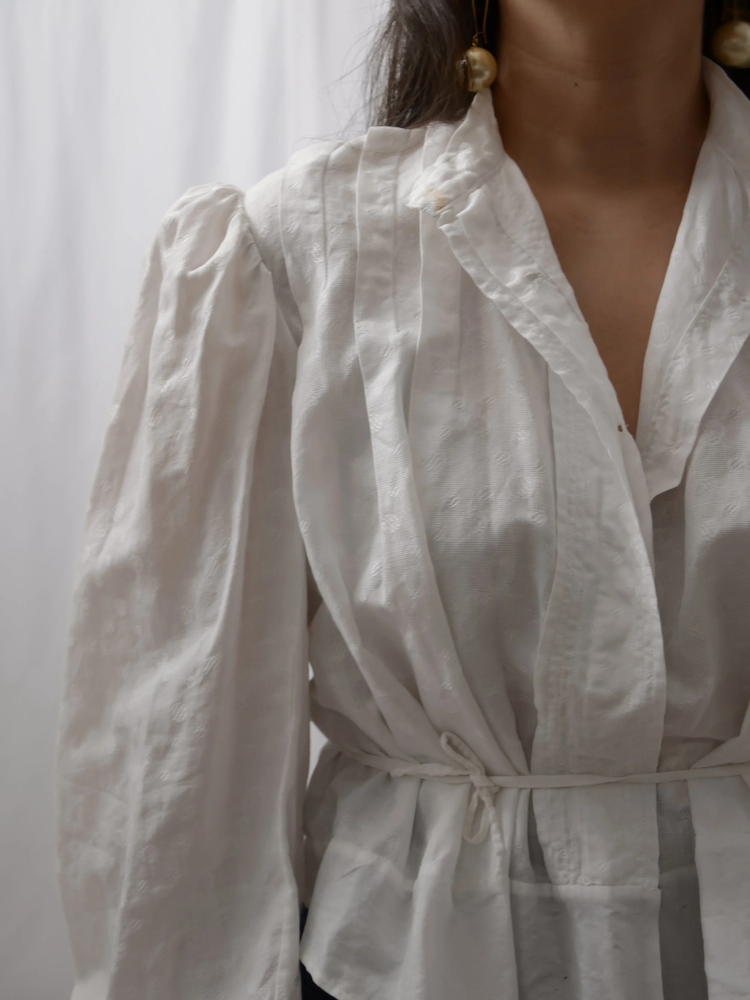 Detail of the 1900s-1910s white cotton blouse's puffed sleeve and button front with pintucks.