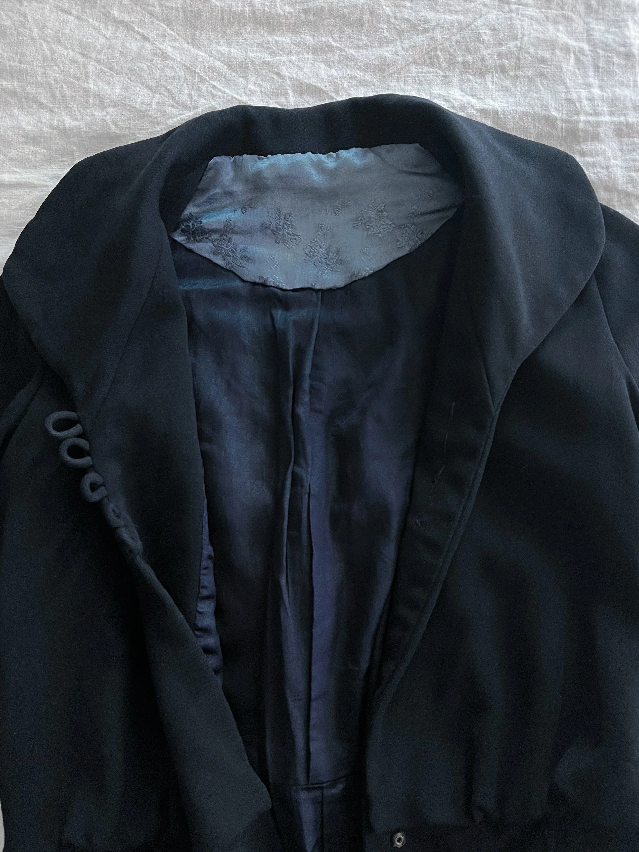 Detail of the Edwardian navy jacket's open front, showing the collar, corded button loops and pale blue silk lining.