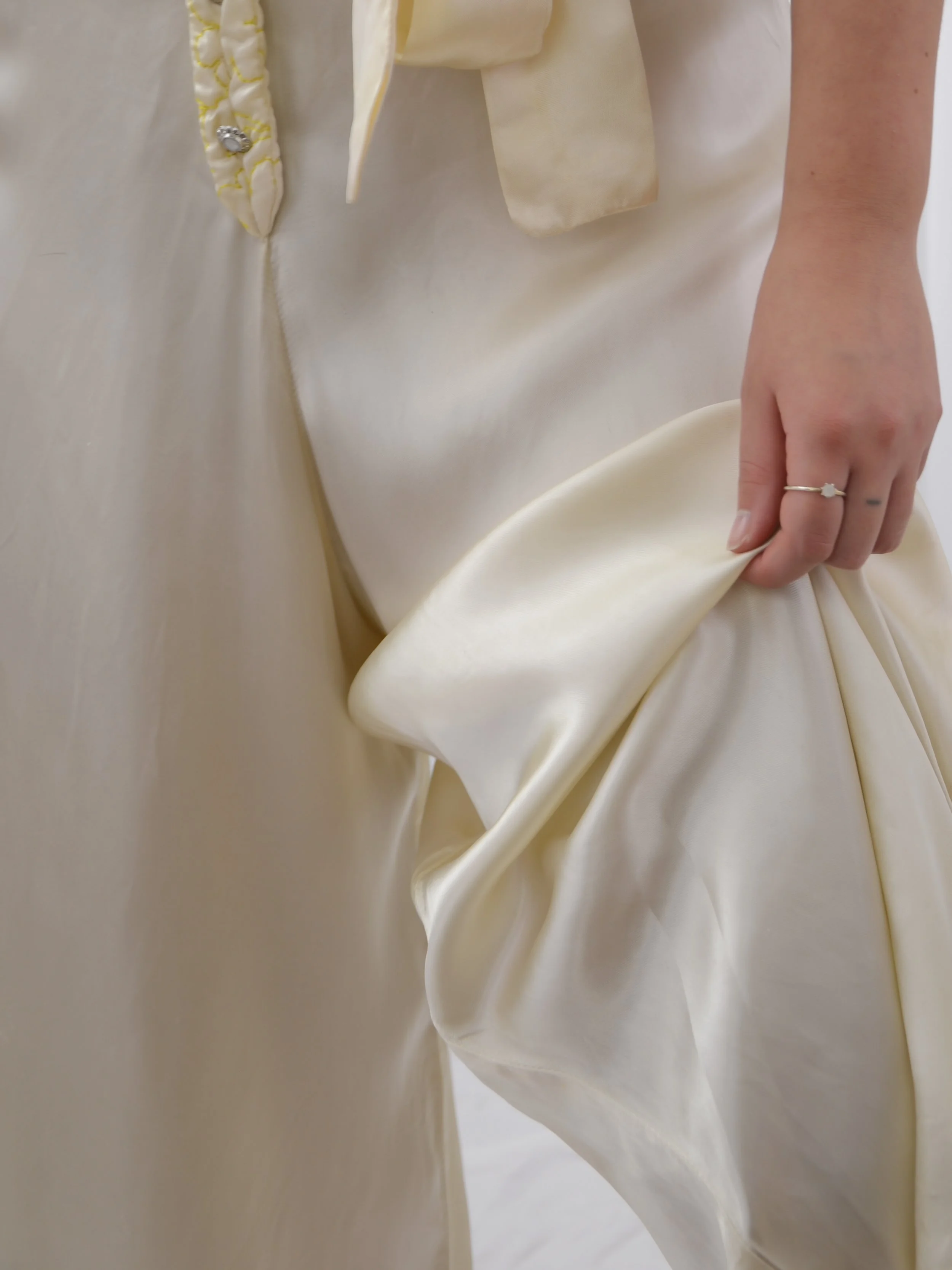 Detail of the 1940s satin jumpsuit's wide leg held out by hand, showing the satin sheen and sash end.