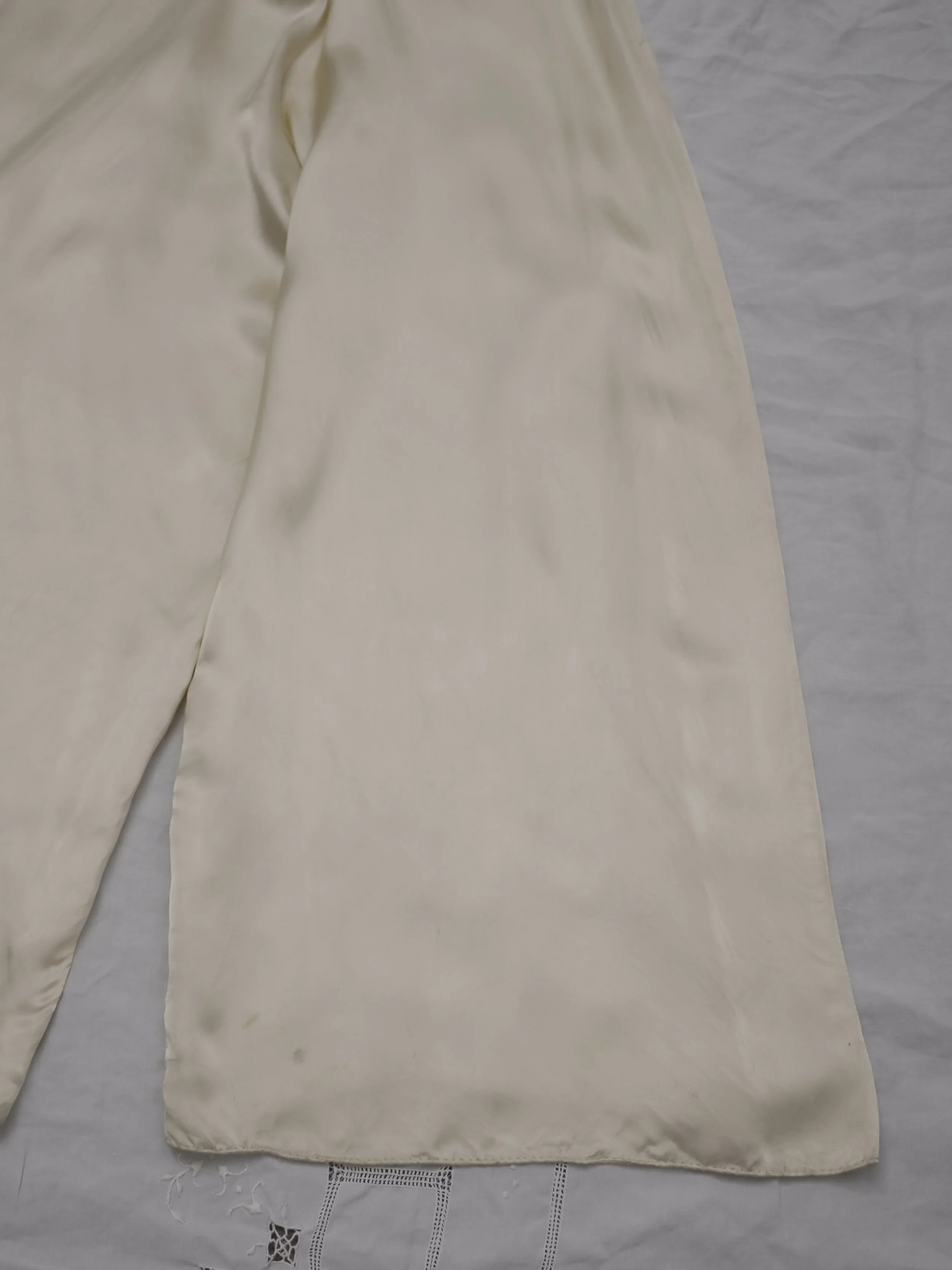 Close-up of the 1940s satin jumpsuit's wide pant hems laid flat on white linen.