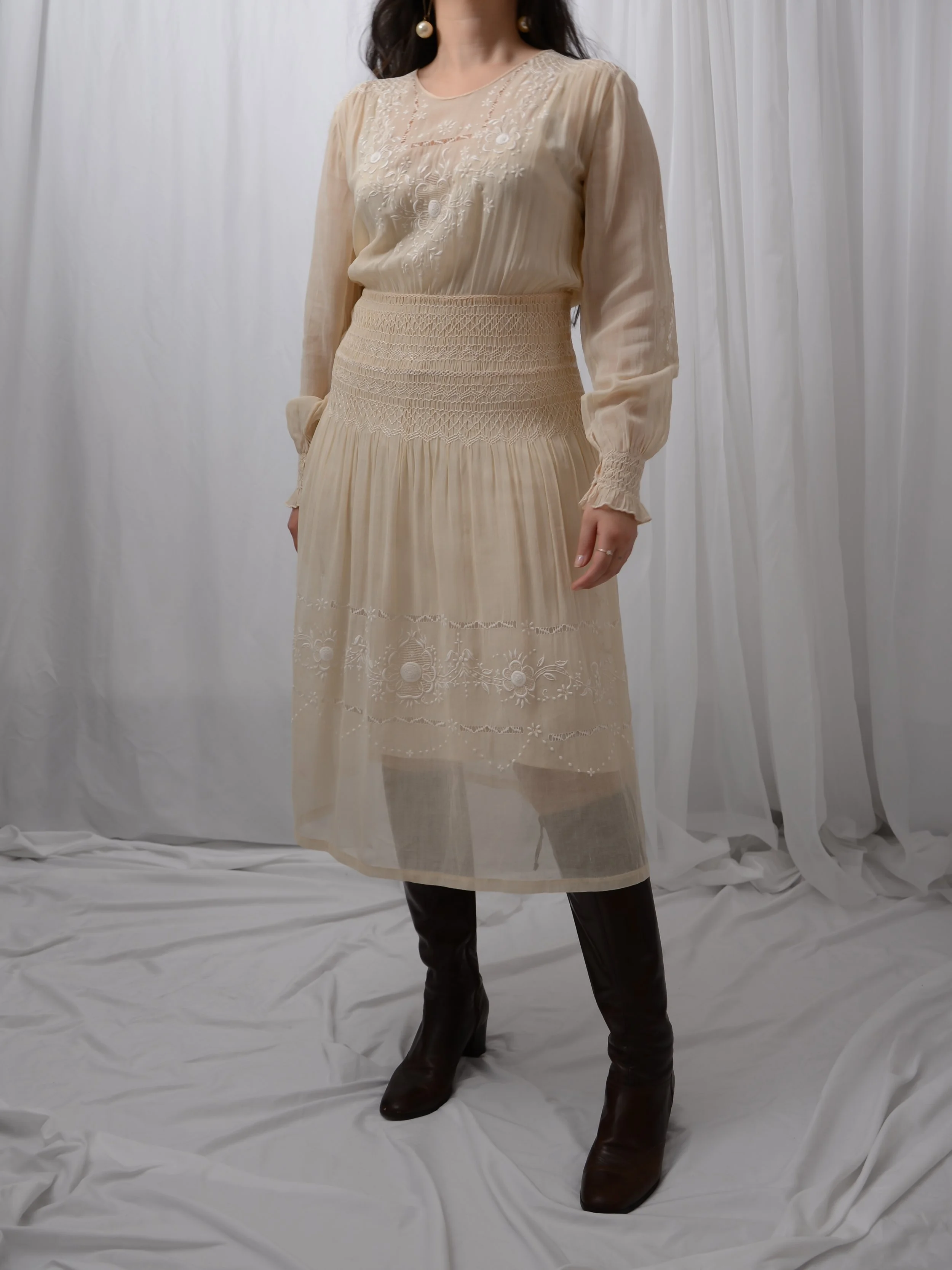 Front view of the 1920s ecru Hungarian smocked dress on a model with tall dark boots.