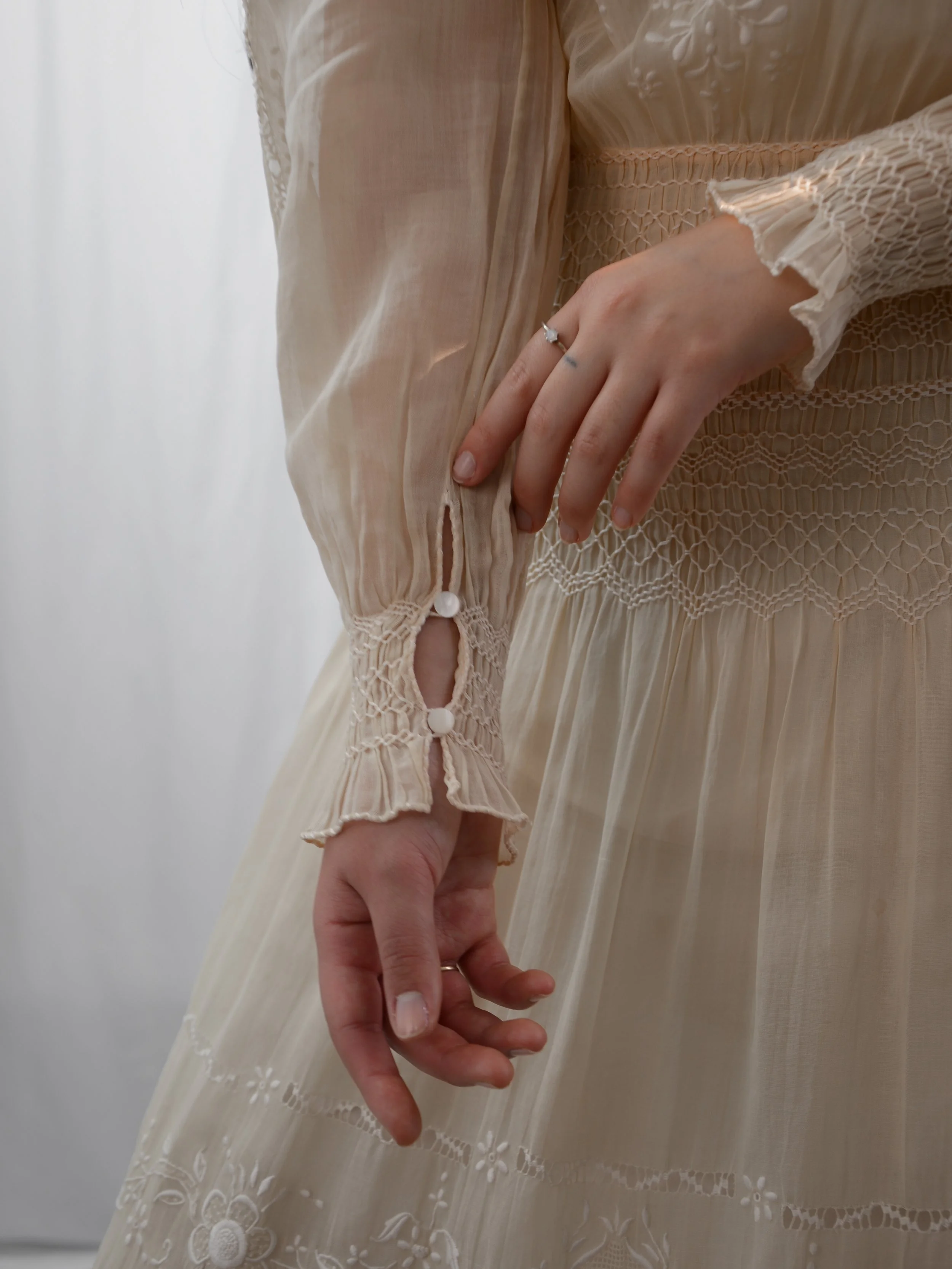 Close-up of the 1920s ecru voile dress's smocked cuff with button and the smocked waist.