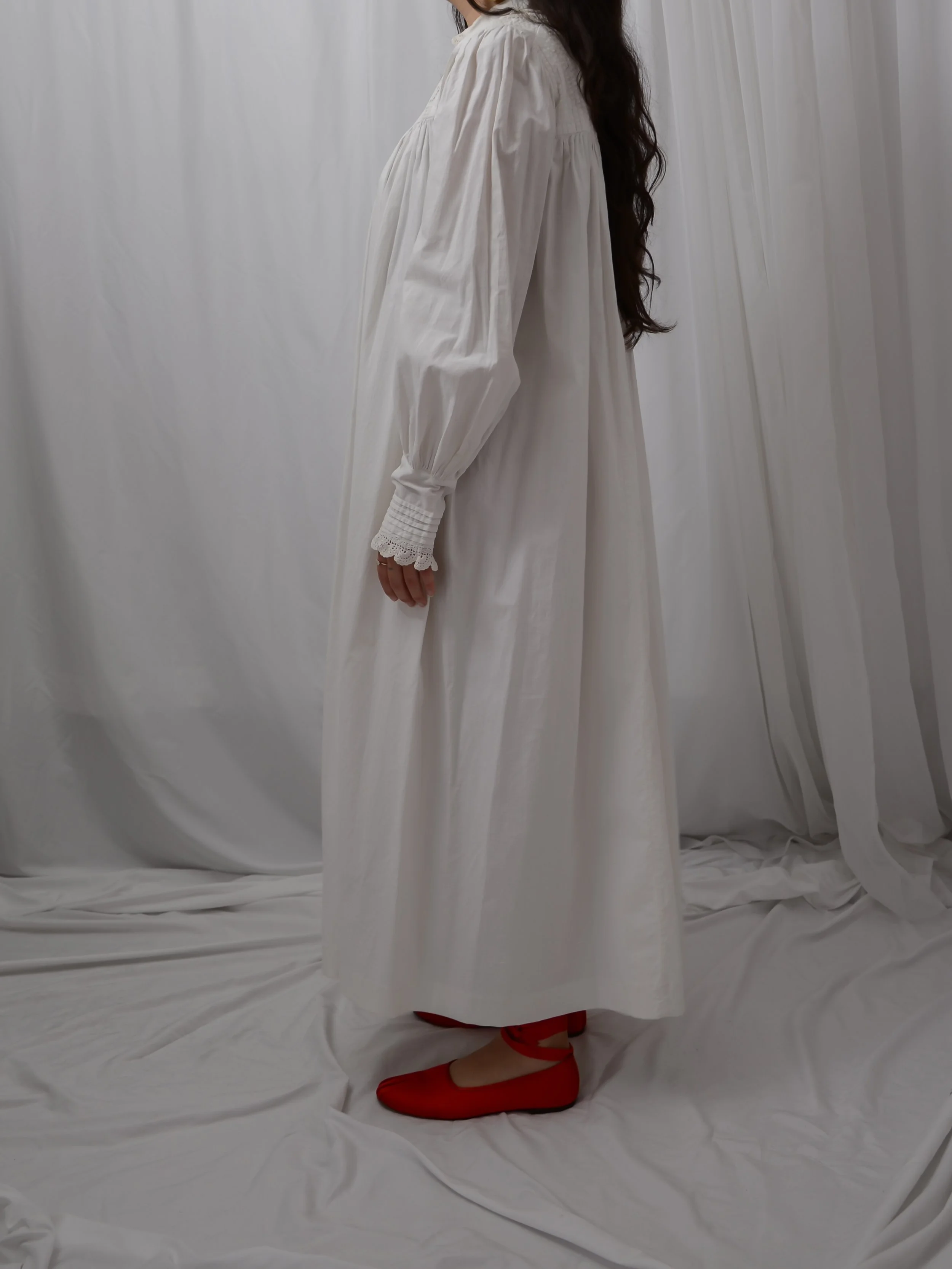 Side view of the circa 1900s white cotton dress on a model, showing the full skirt and lace cuffs.