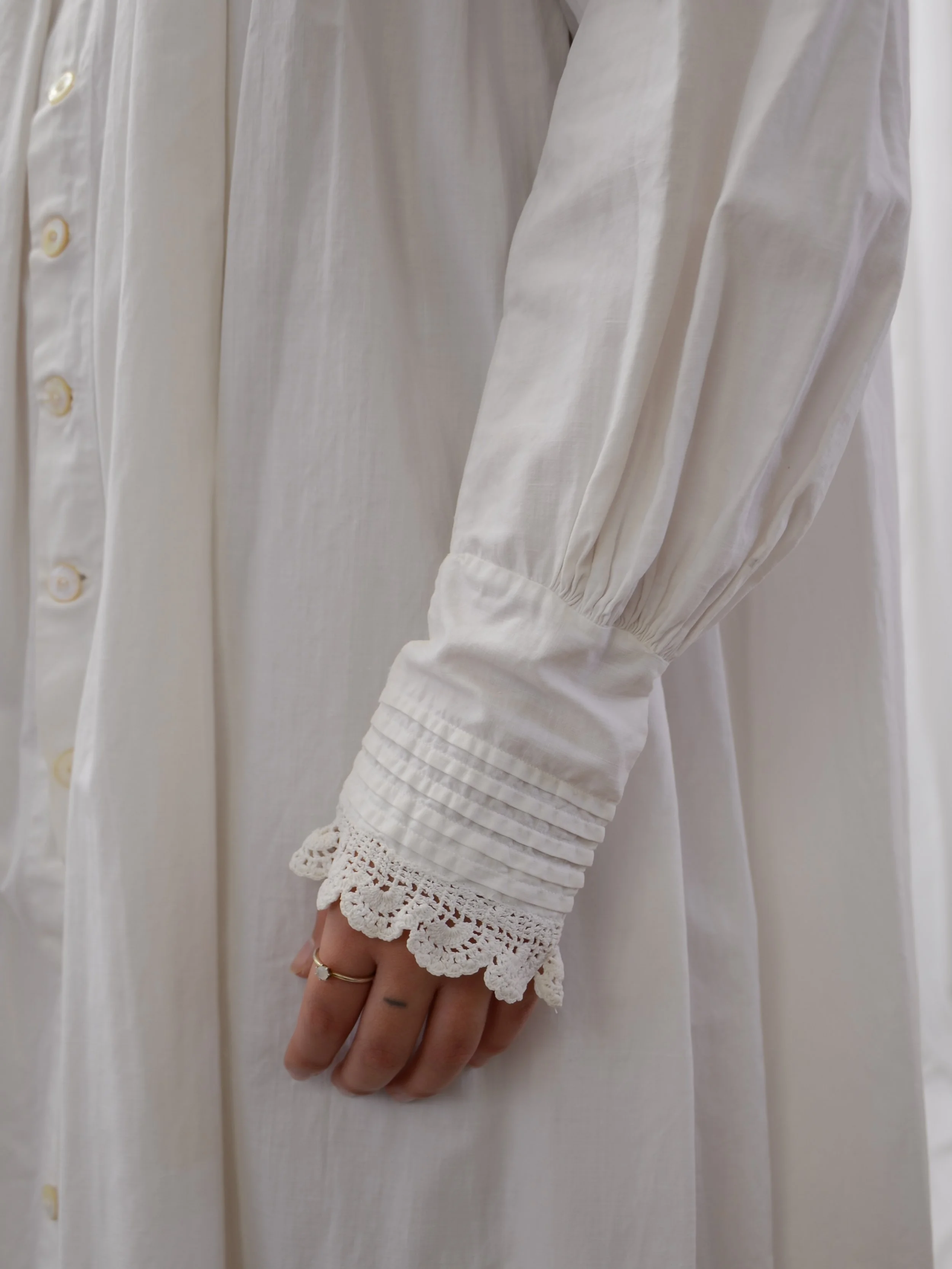 Detail of the antique white cotton dress's gathered sleeve and pintucked cuff with scalloped lace edge.
