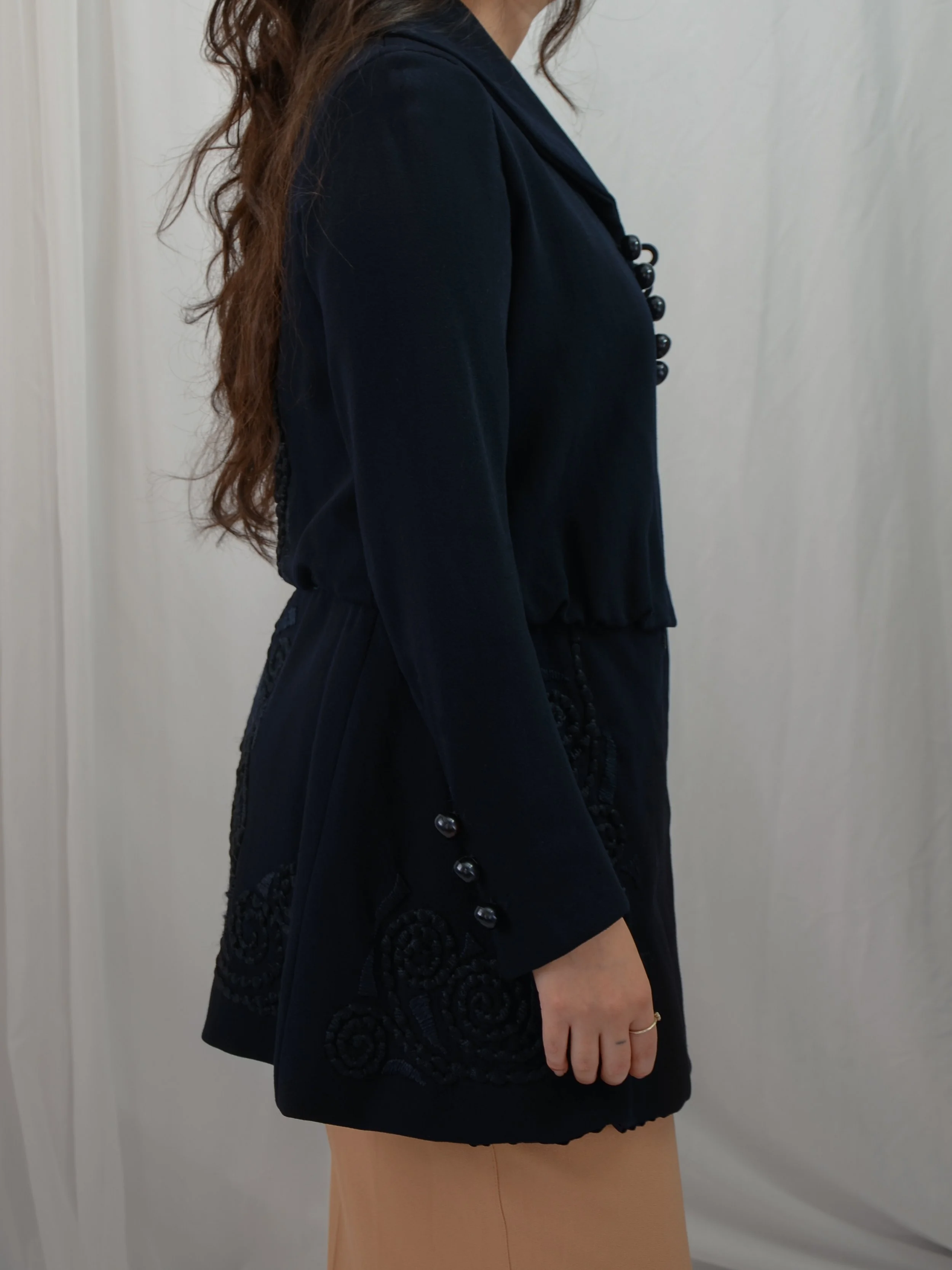 Side view of the Edwardian navy walking jacket on a model, showing button cuffs and swirling hip embroidery.