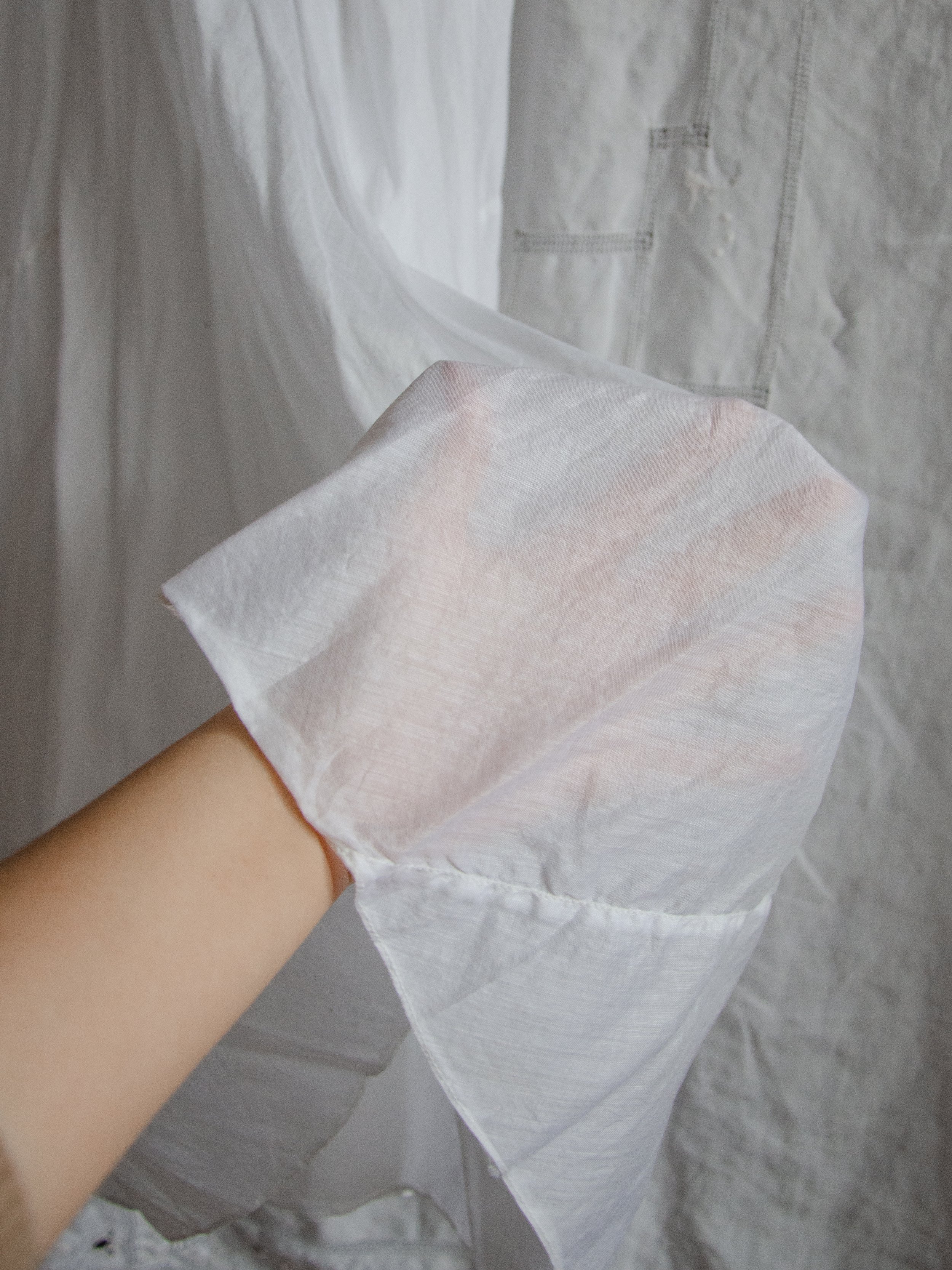 Detail of the 1940s white cotton slip dress fabric held over a hand, showing its lightweight sheerness.