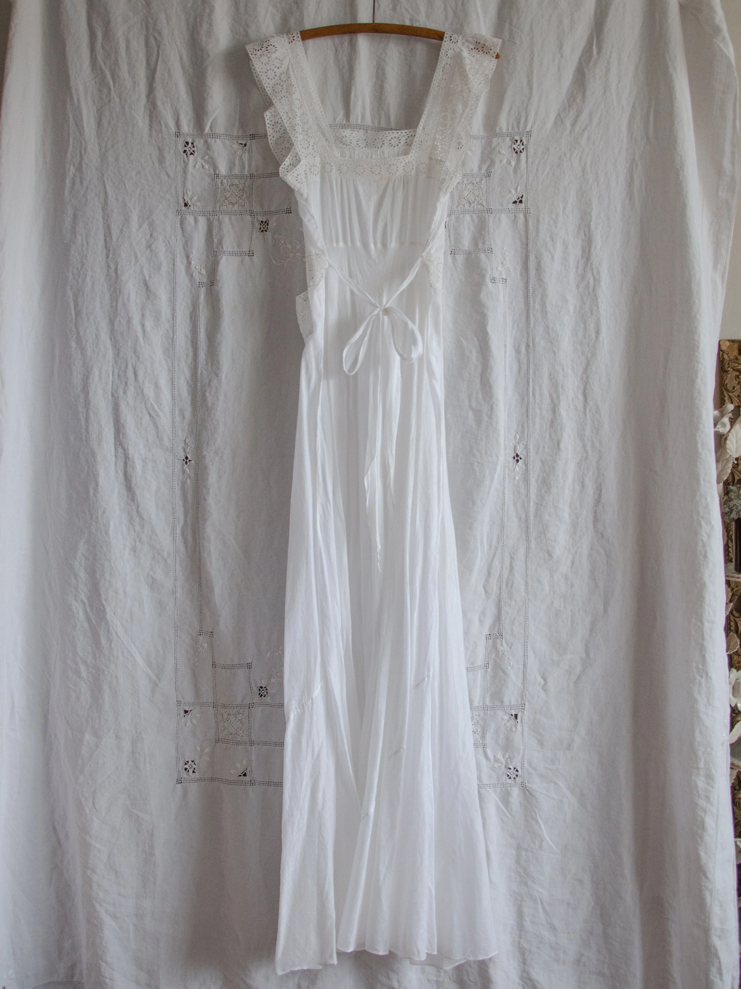 Full-length back view of the 1940s white bias-cut slip dress on a hanger, showing the bow tie at the waist.