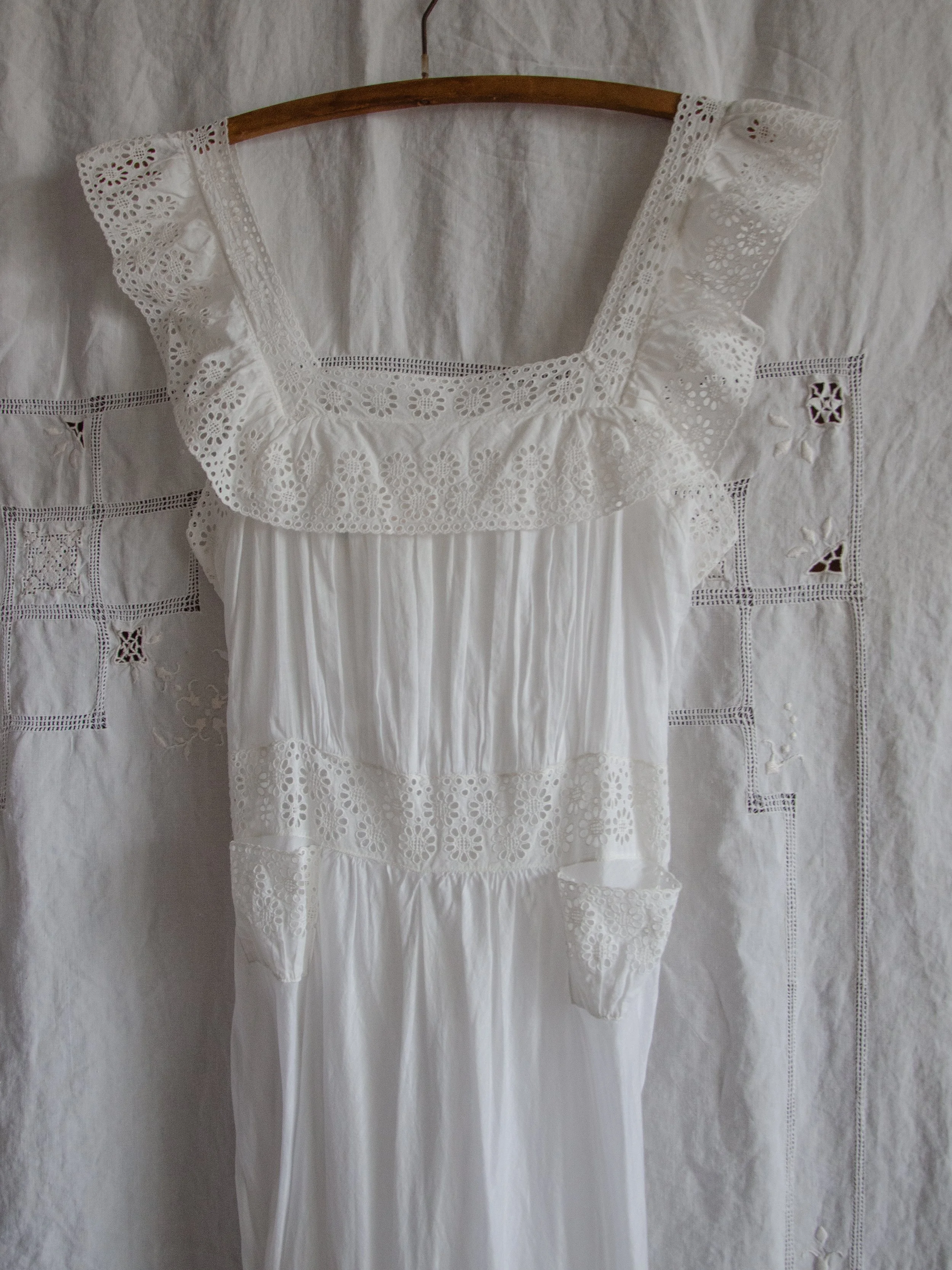Front view of the 1940s white cotton slip dress bodice on a hanger, showing eyelet ruffles and tiny hip pockets.