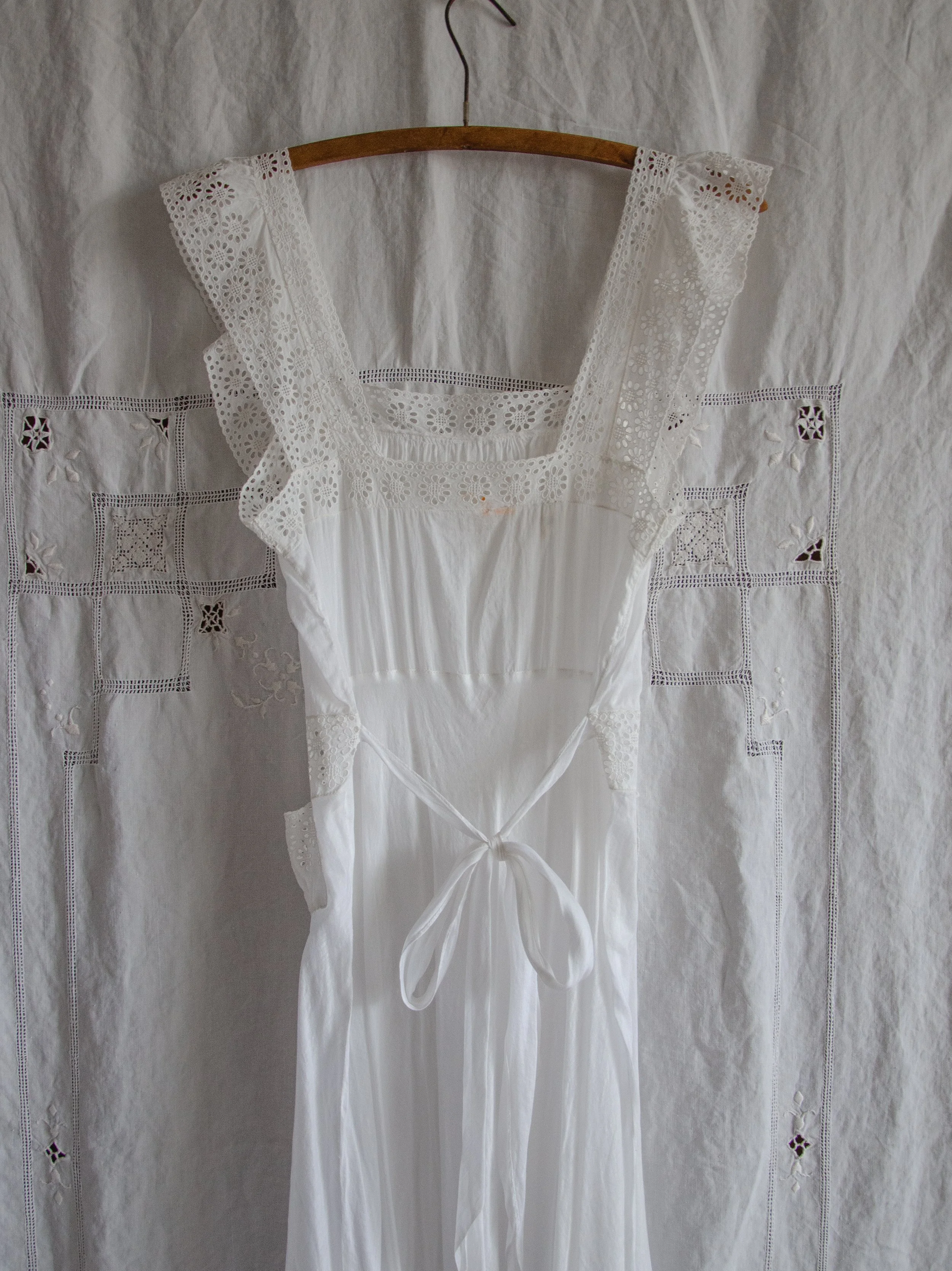 Back view of the 1940s white cotton eyelet slip dress on a hanger, showing the eyelet straps and waist tie.