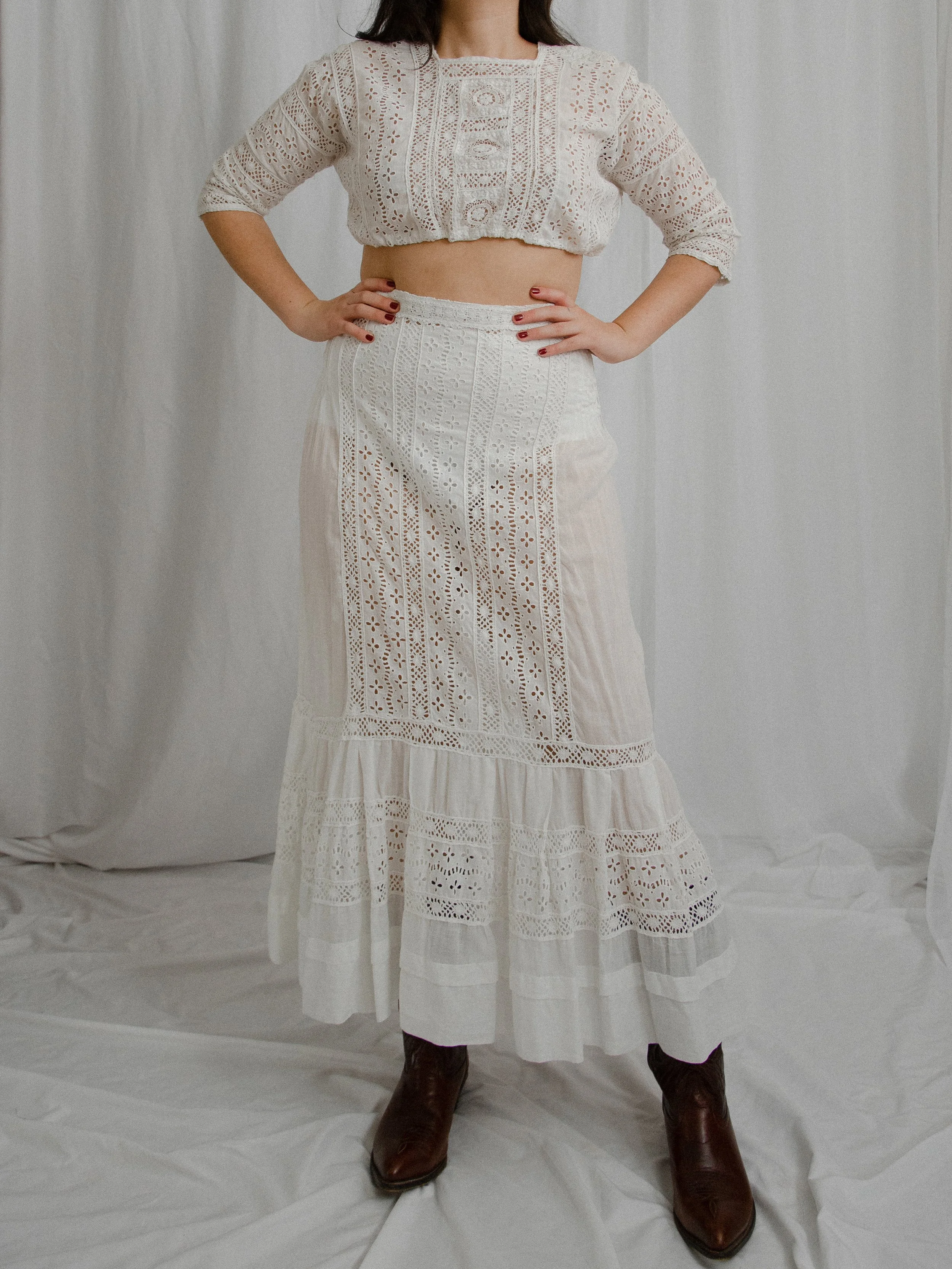 Front view of the Edwardian white eyelet two-piece set on a model with hands on hips and brown boots.