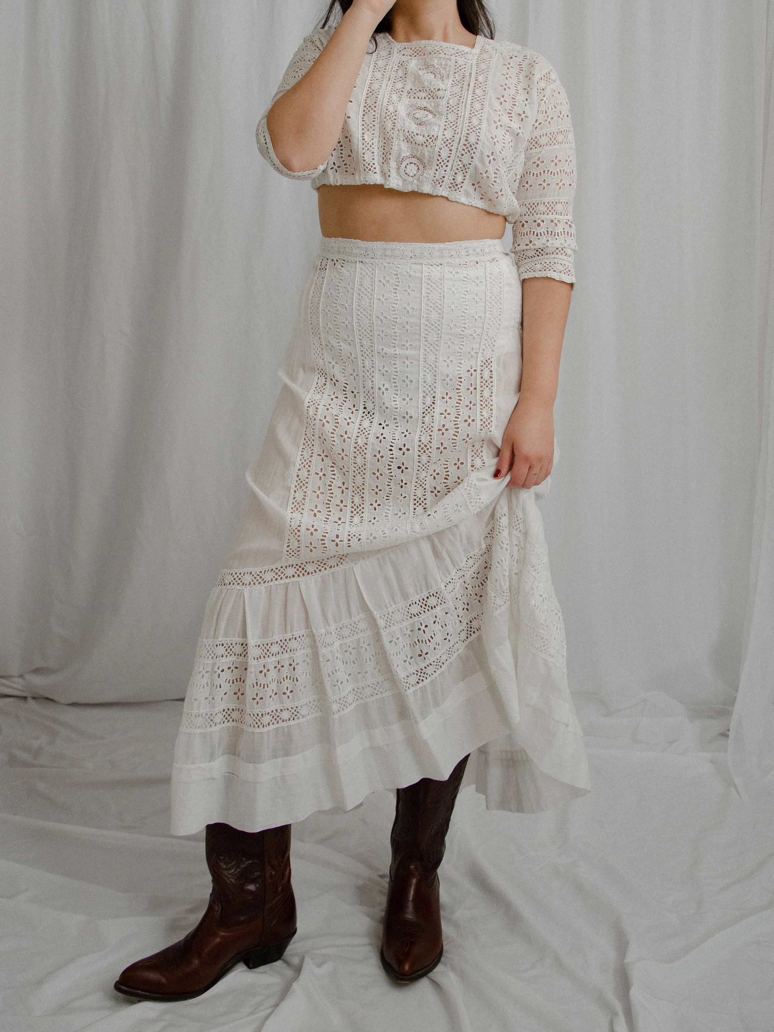 Edwardian white eyelet set on a model holding up the skirt to show its high-low ruffled hem.