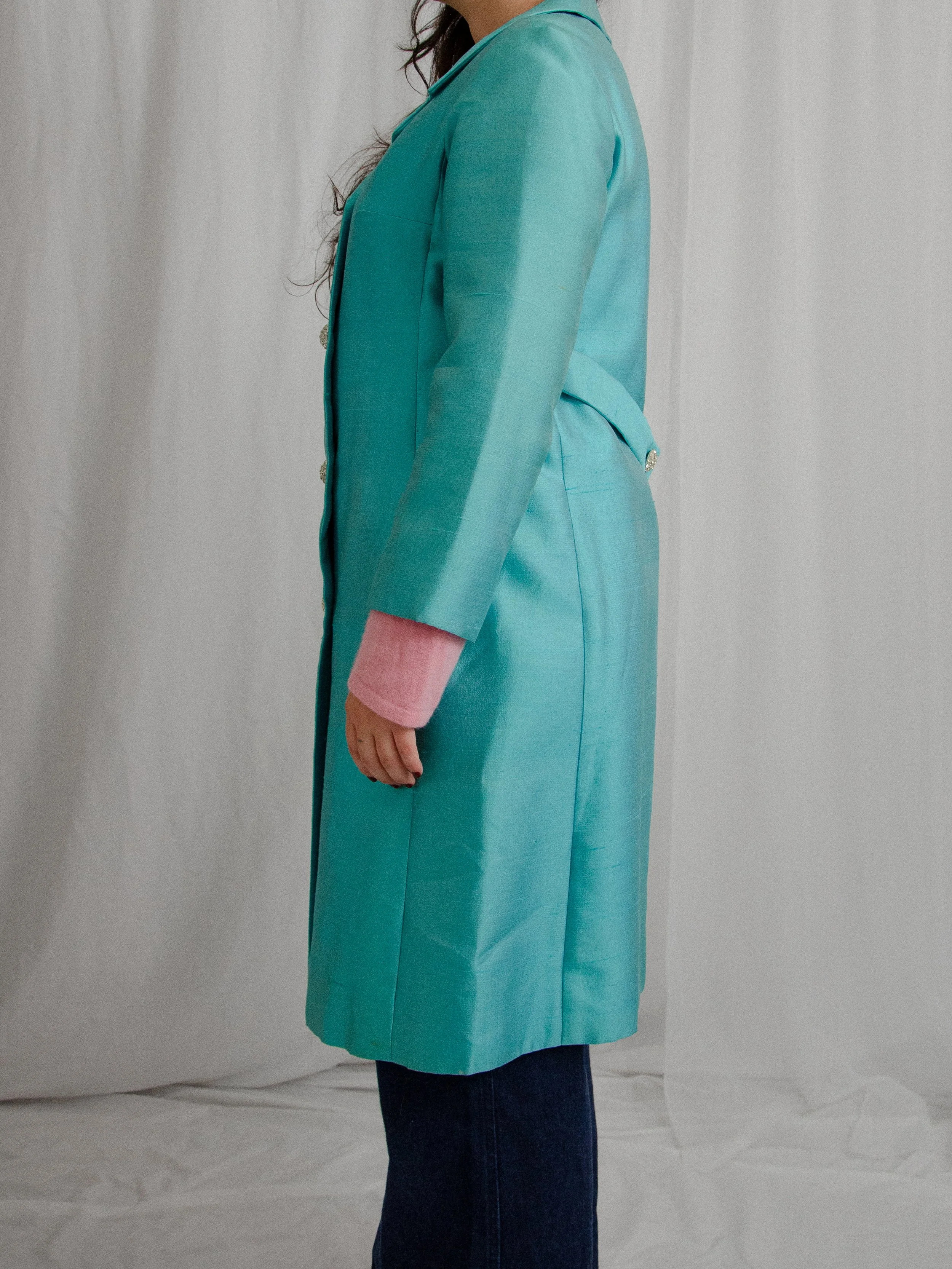 Side view of the 1960s aqua blue silk coat on a model, showing the knee length and back belt.