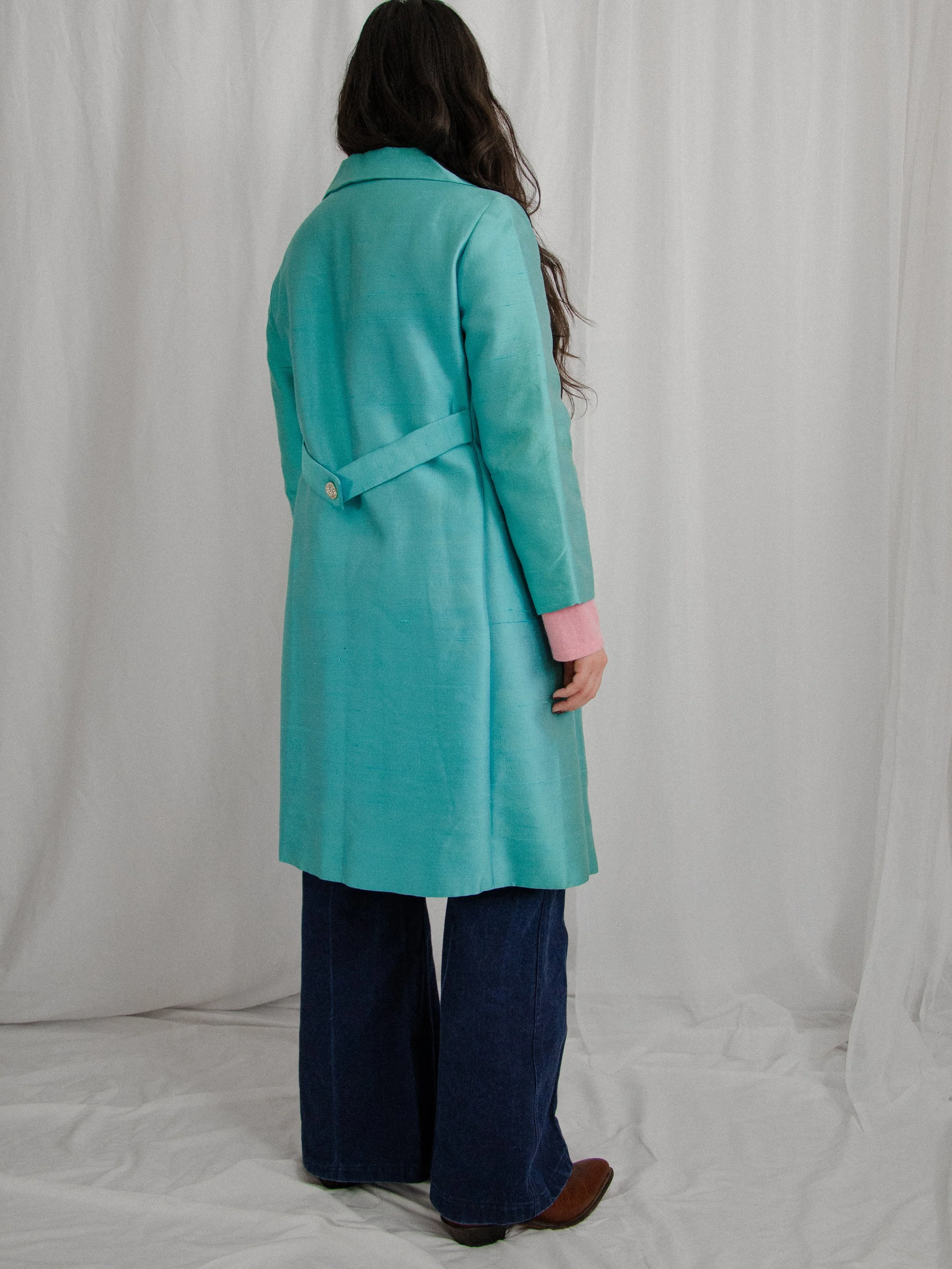 Back view of the early 1960s aqua silk coat on a model, showing the half belt at the back waist.