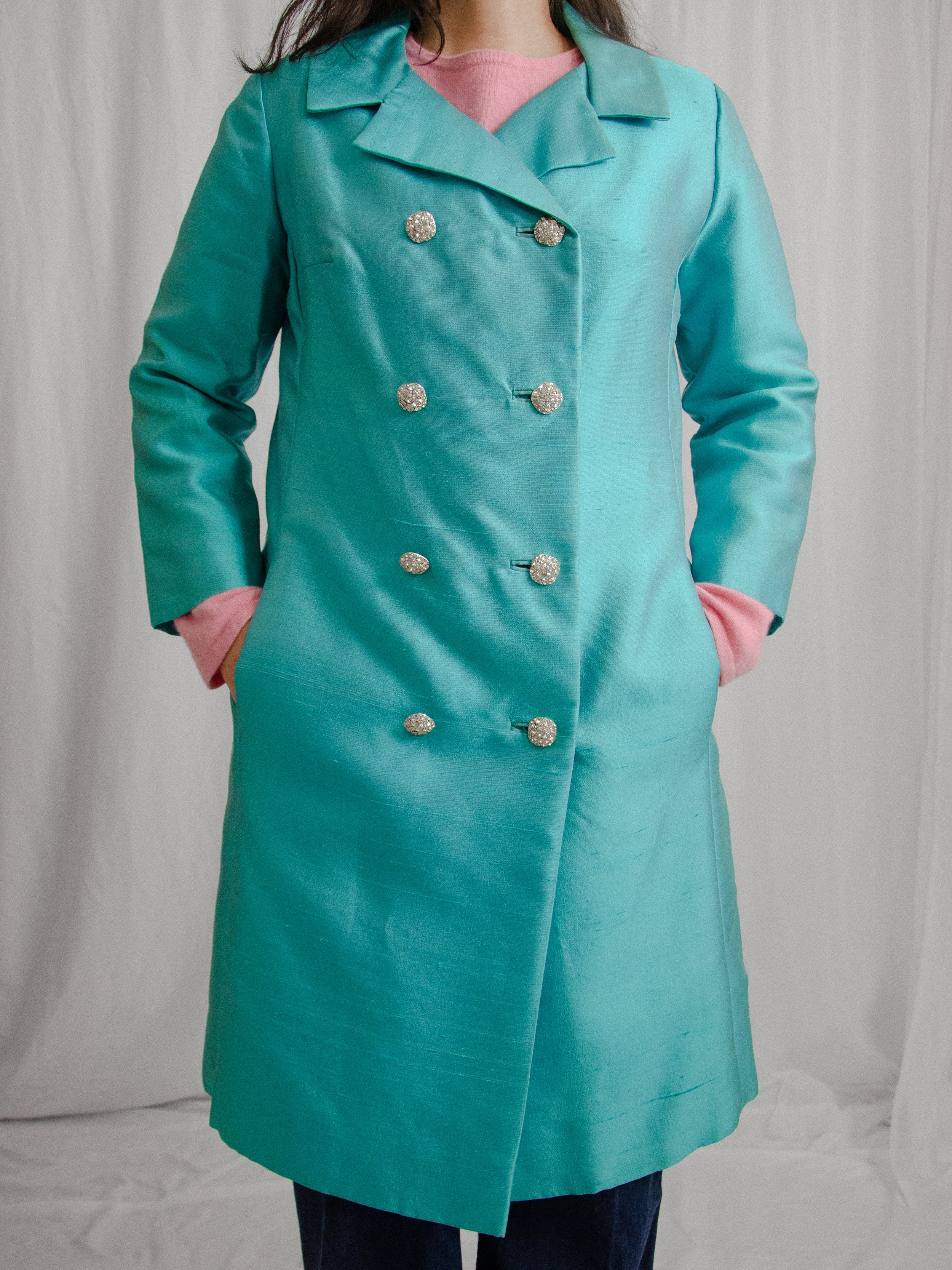 Front view of the early 1960s aqua dupioni silk coat buttoned on a model, hands in pockets.
