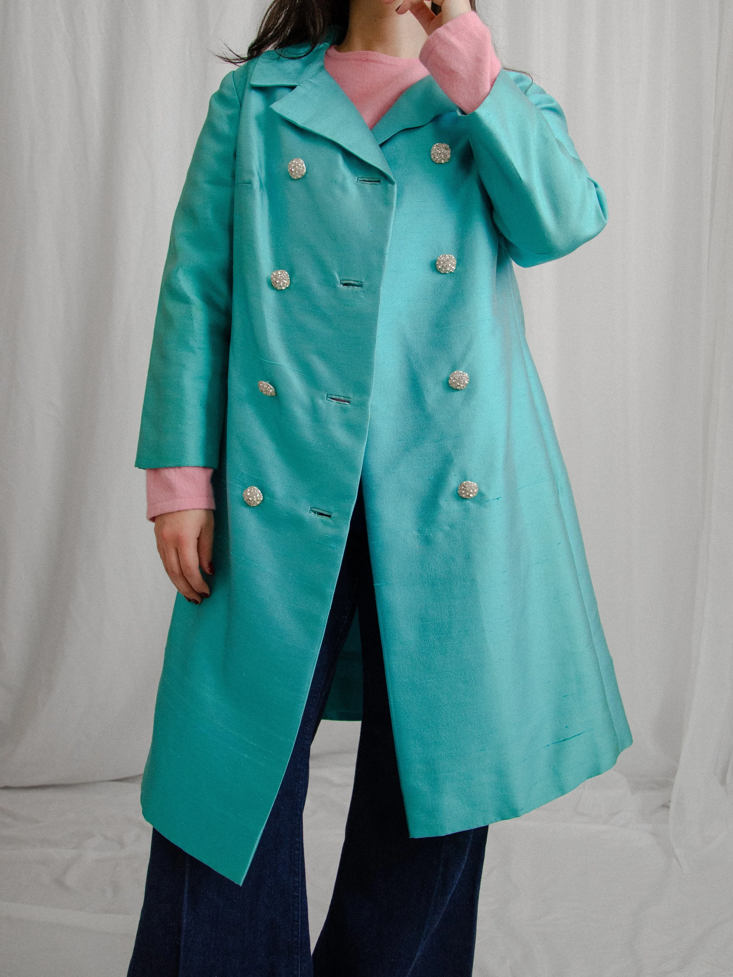 Early 1960s aqua blue silk coat worn open on a model over a pink sweater and wide-leg jeans.