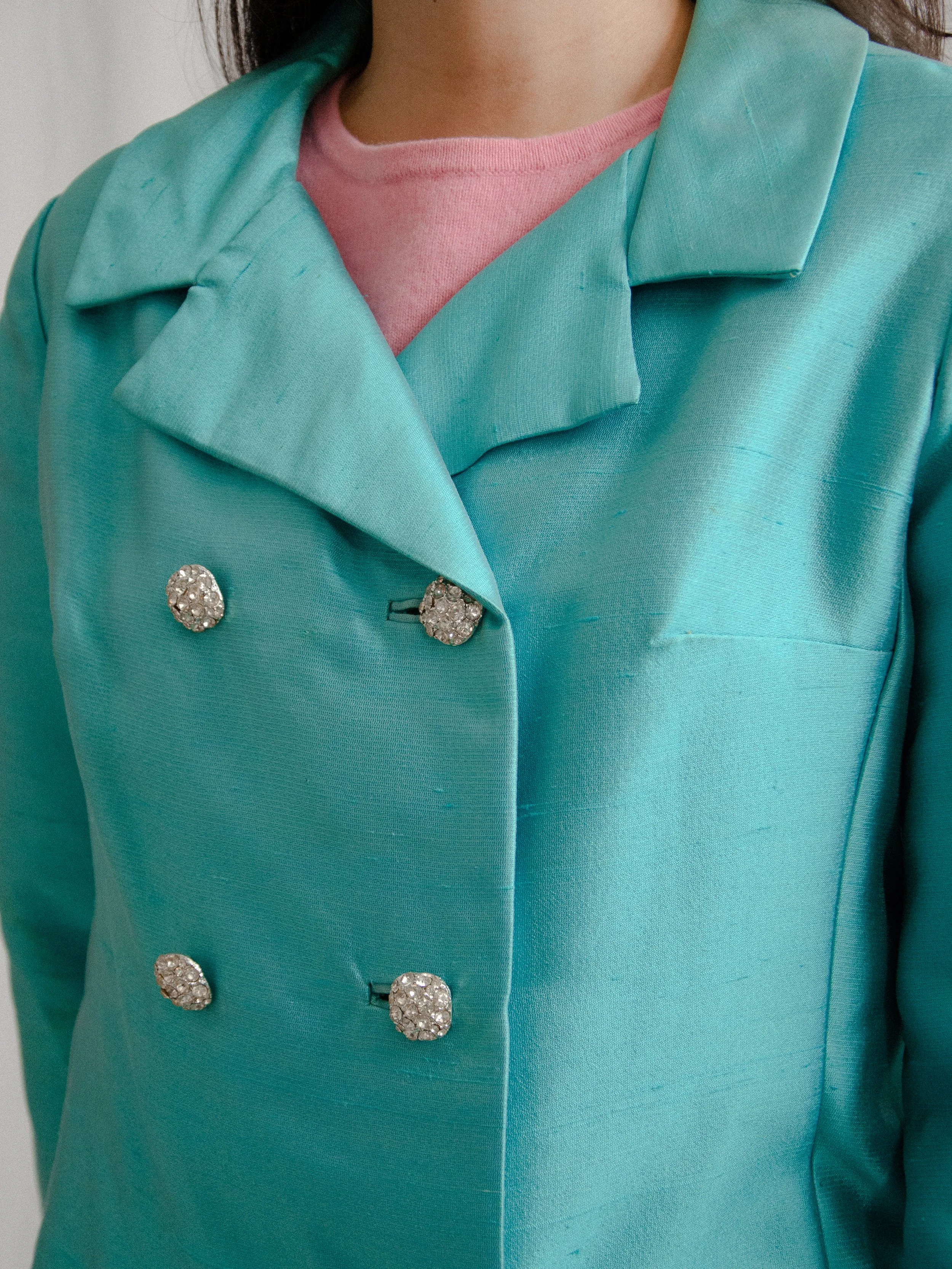 Close-up of the 1960s aqua silk coat's notched collar and sparkling rhinestone buttons.