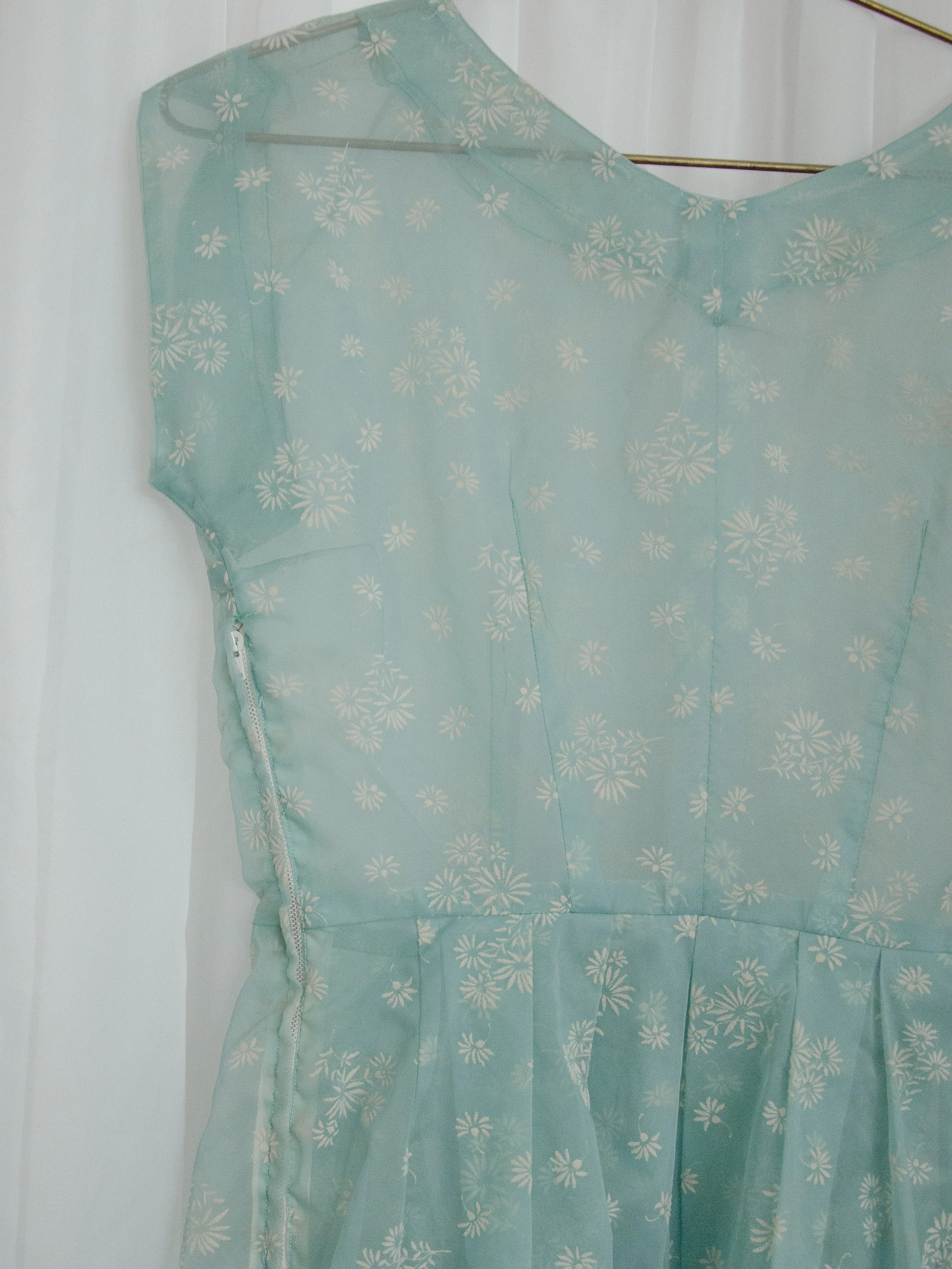 Close-up of the 1950s sheer blue dress bodice on a hanger, showing the V-back and flocked daisies.