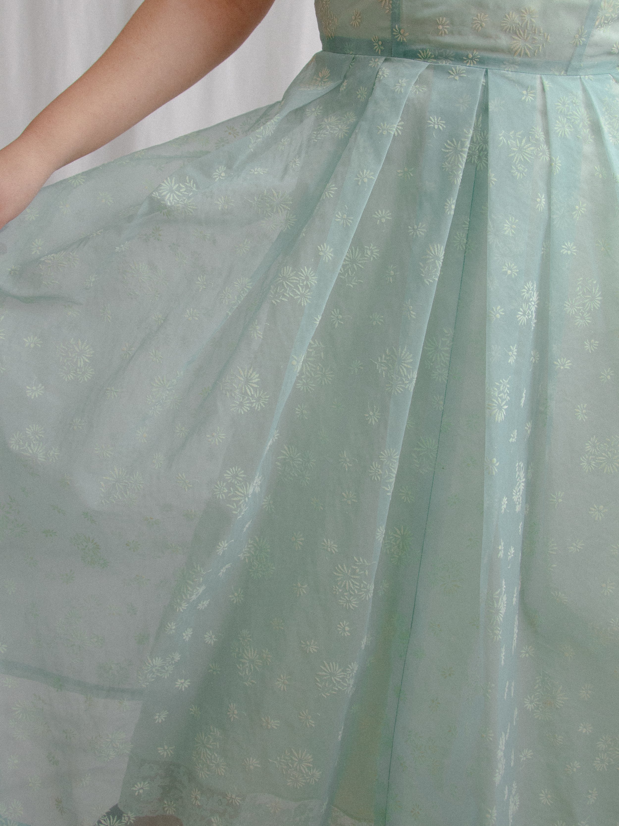 Detail of the 1950s sheer blue daisy dress skirt held out, showing pleats and white flocked flowers.