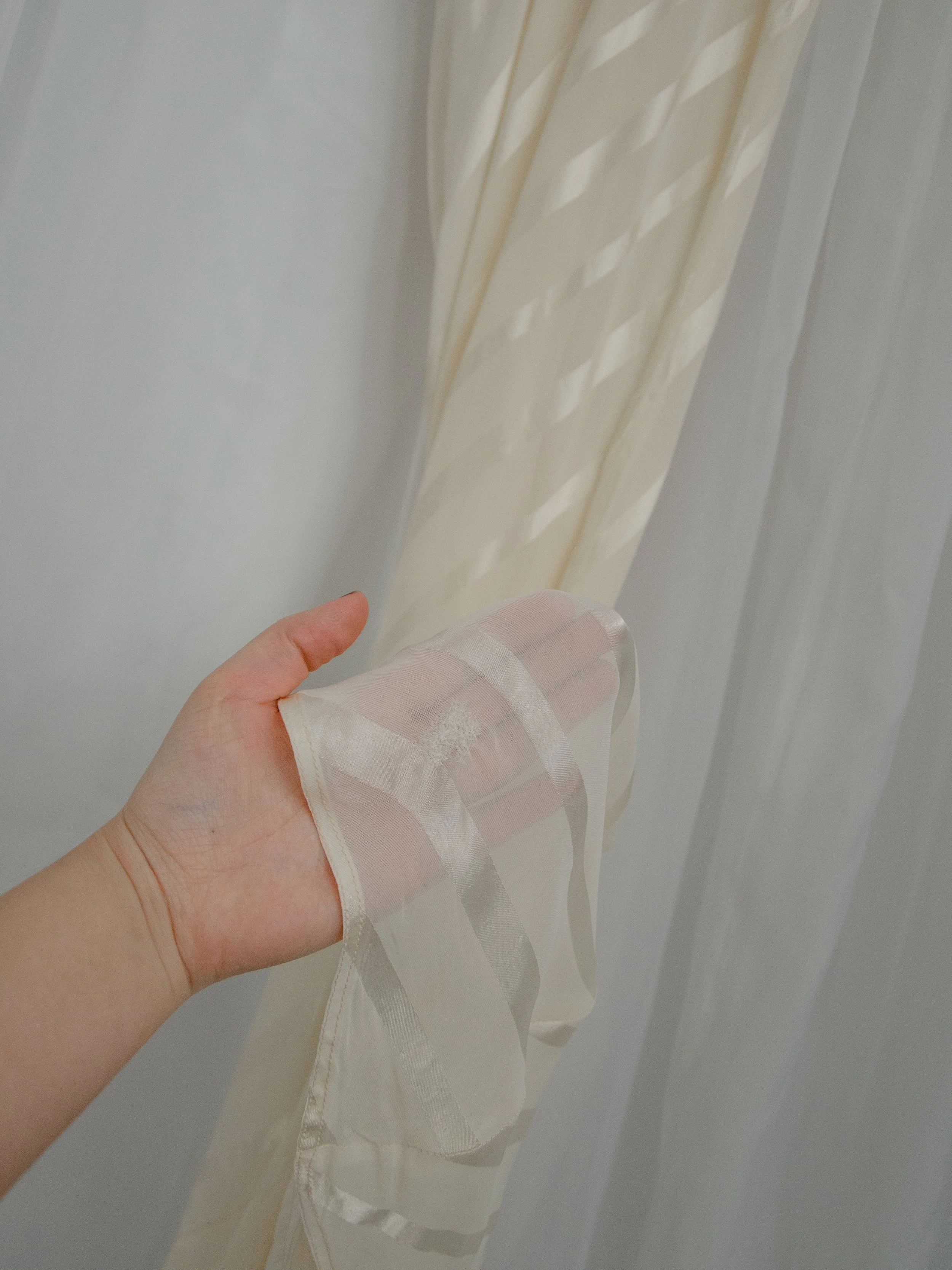 Detail of the 1940s ivory slip dress hem held in hand, showing the semi-sheer nylon with satin stripes.