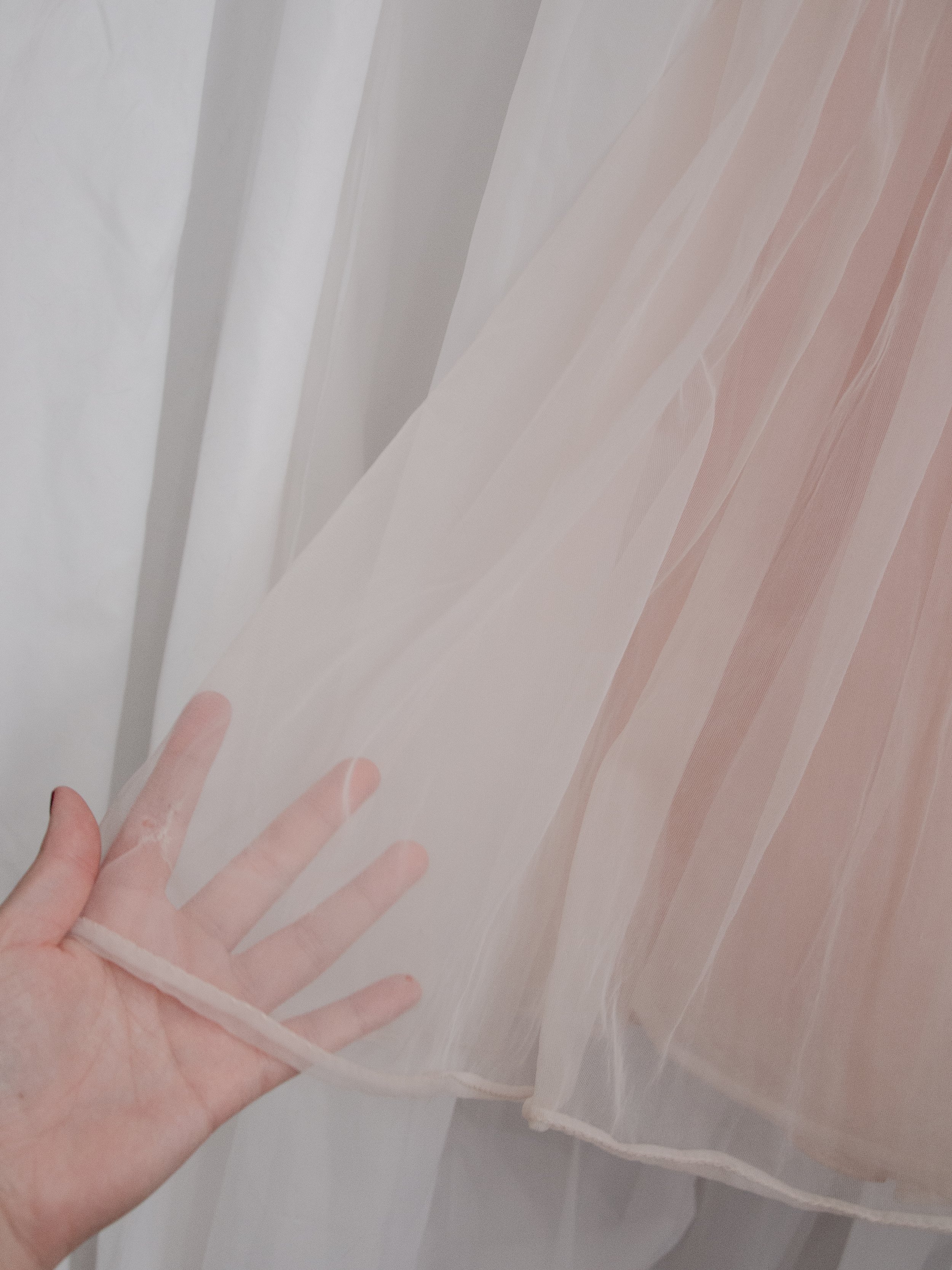 Detail of the 1950s pink ballerina dress hem held over a hand, showing the sheer double nylon layers.