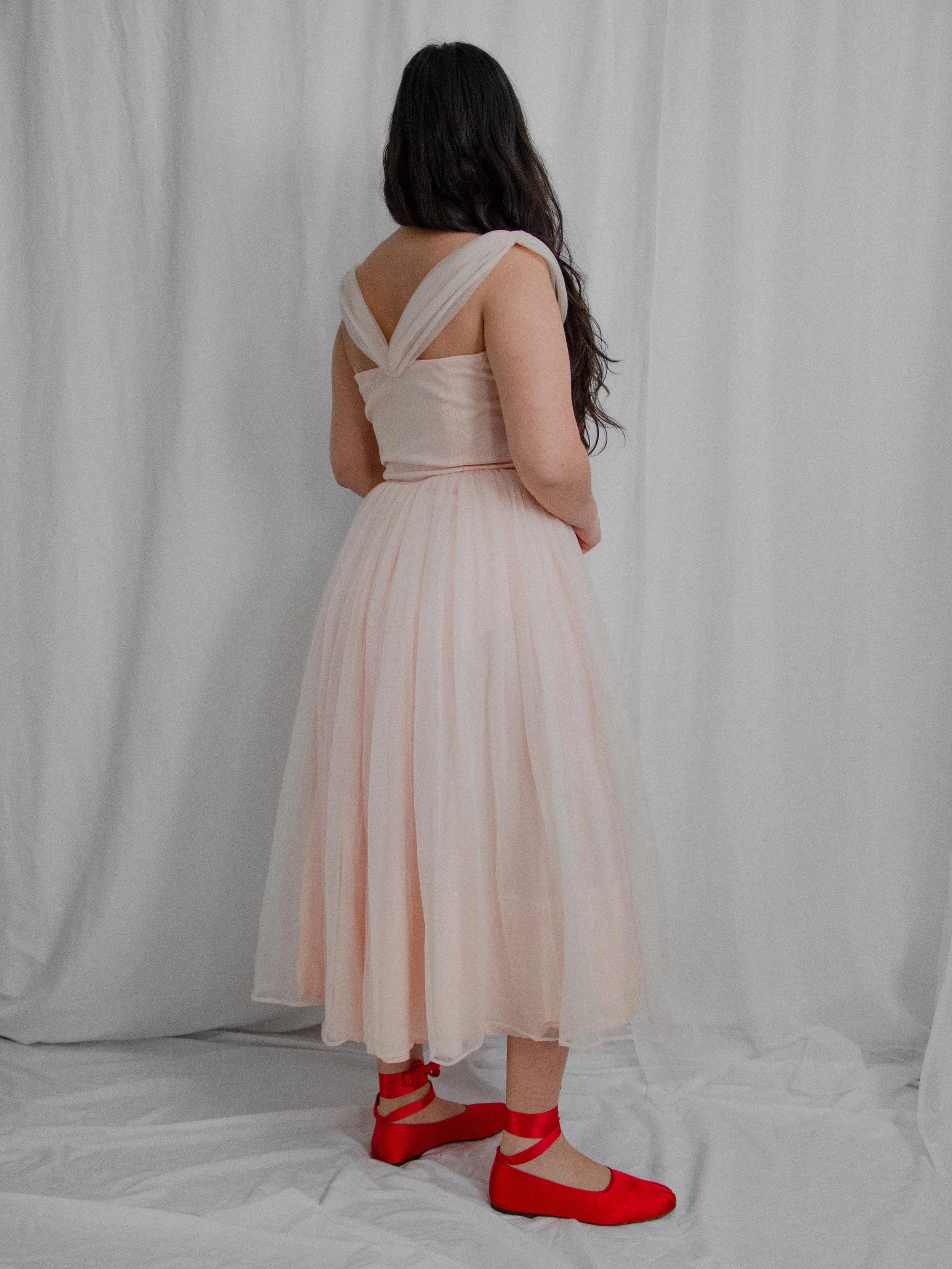 Back view of the 1950s baby pink ballerina dress on a model, showing the crossed straps and full skirt.