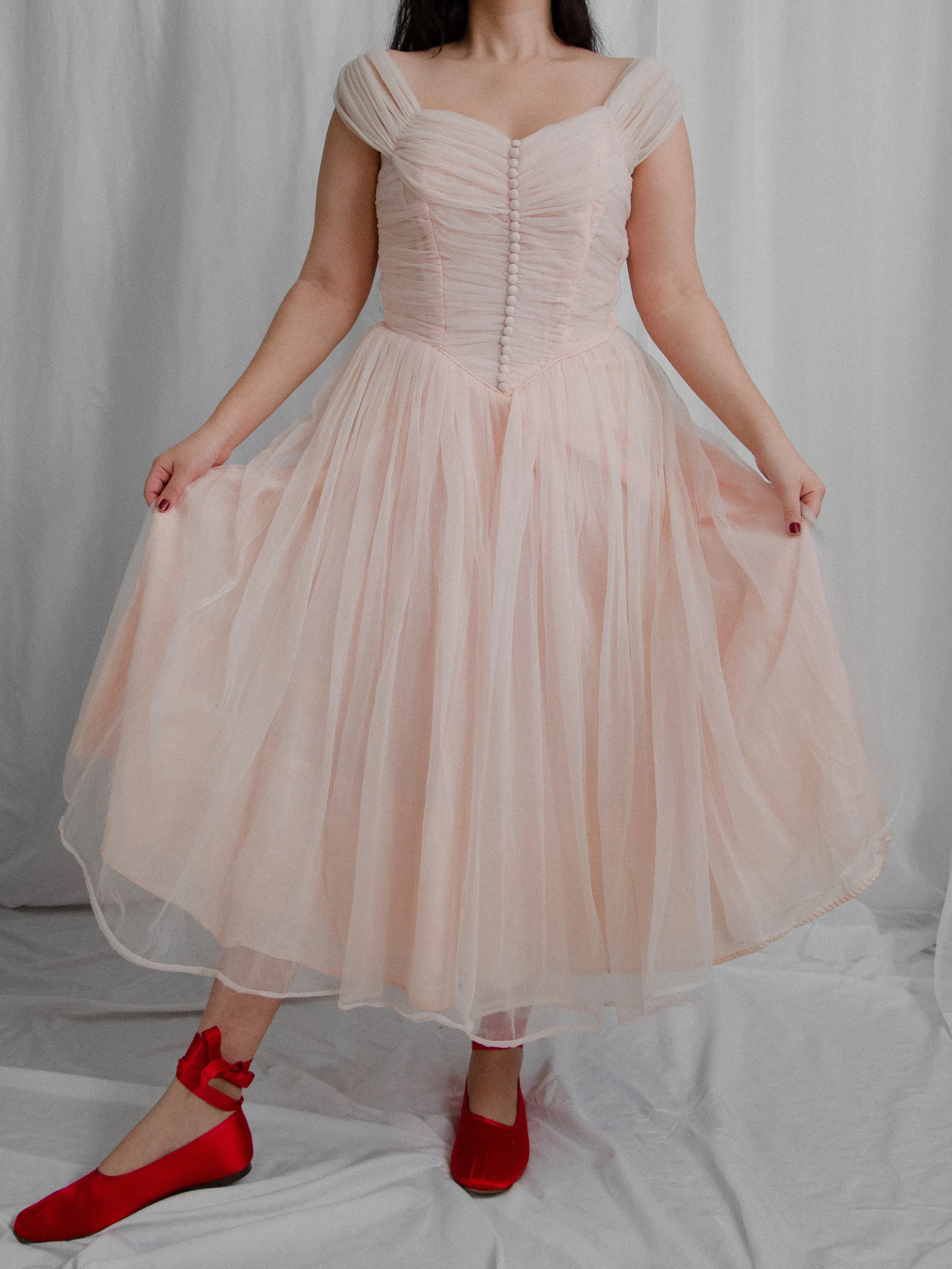 1950s baby pink ballerina dress on a model holding out the full layered nylon skirt.