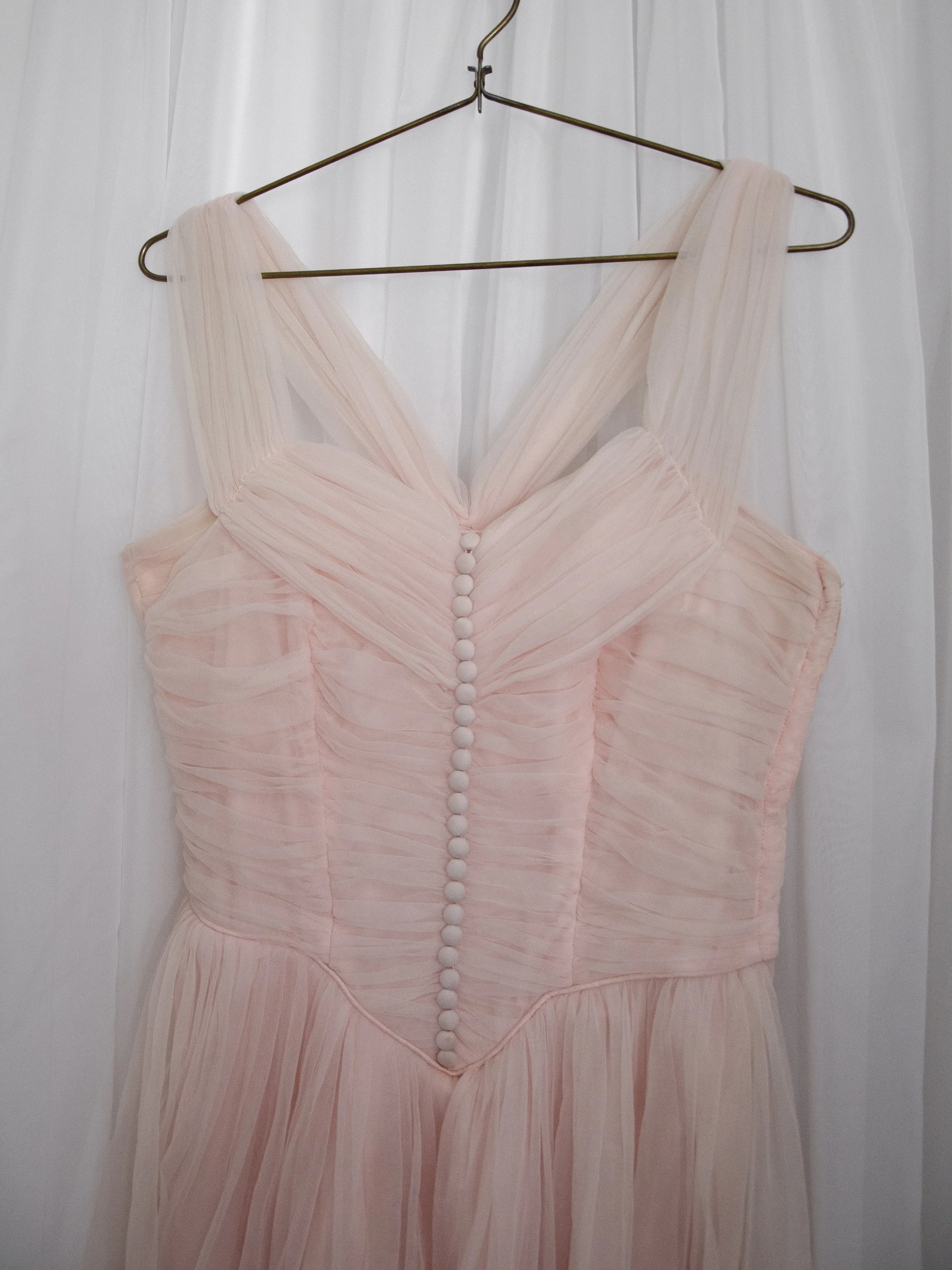 1950s baby pink ballerina dress on a hanger with straps up, showing the ruched bodice and buttons.