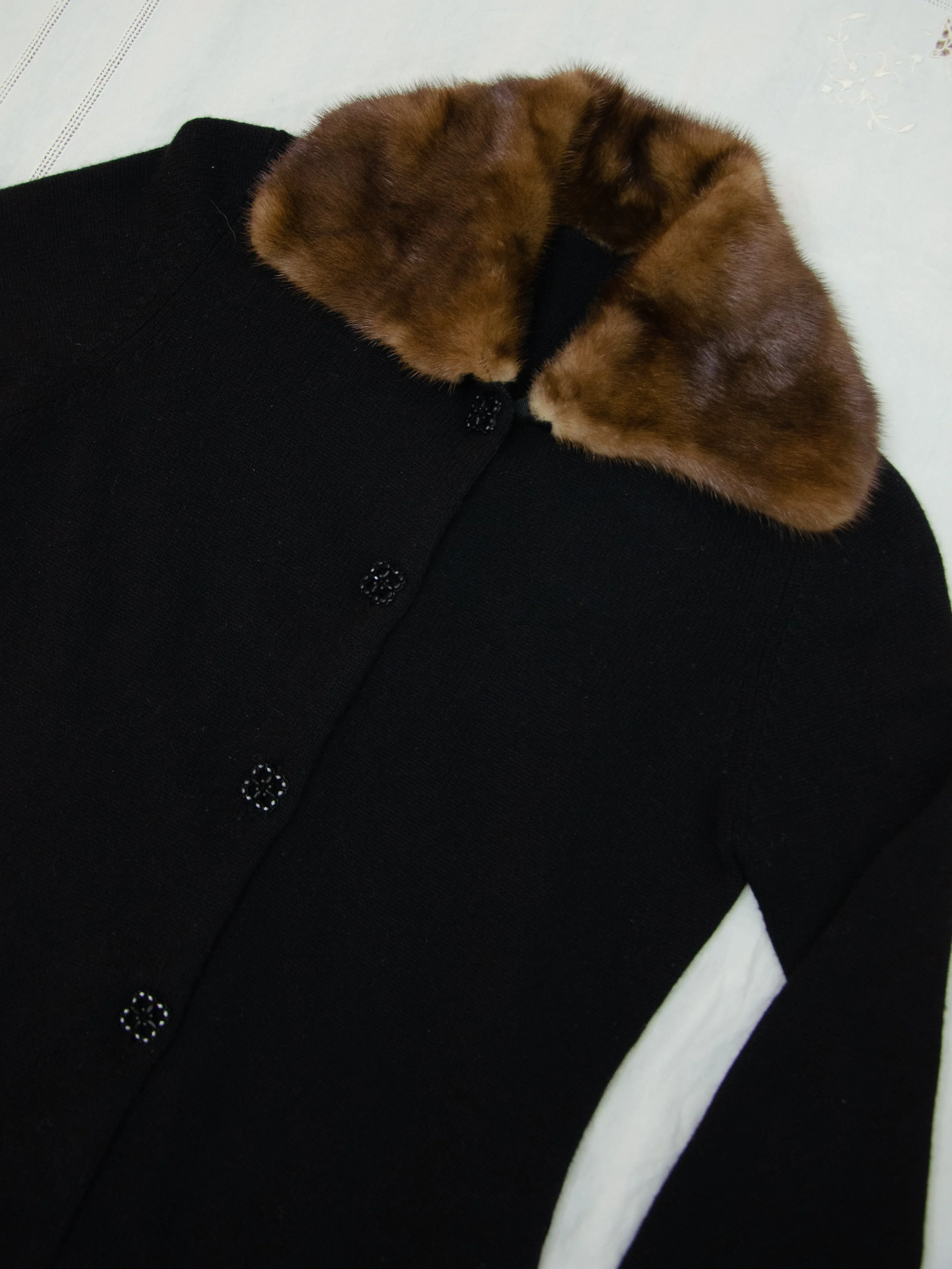 Detail of the 1940s cardigan's mink fur collar and sparkly black buttons, laid flat.