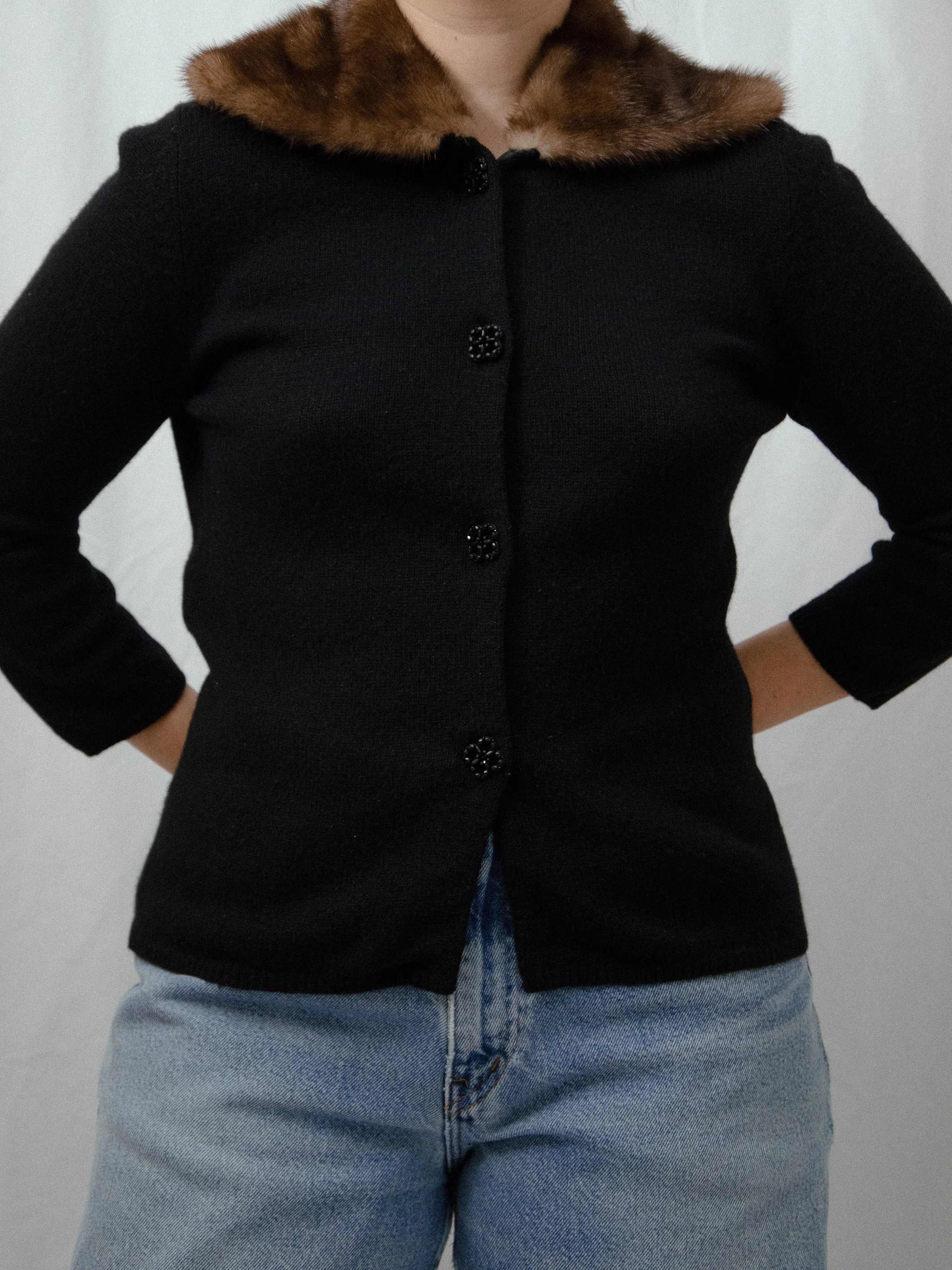 Front view of the 1940s black cardigan with mink collar buttoned on a model with hands on hips.