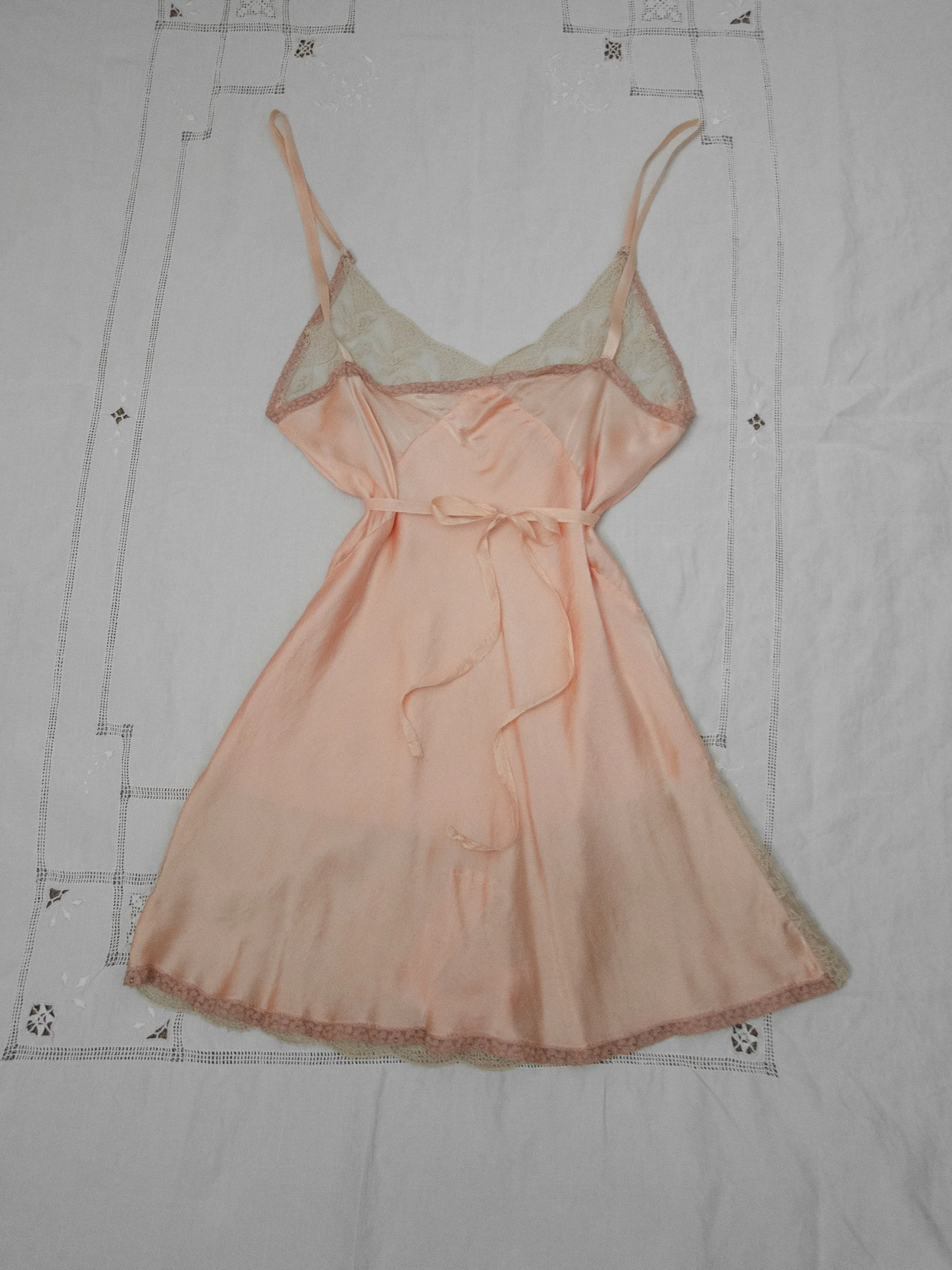 Back view of the 1930s blush silk teddy laid flat, showing ribbon straps and the waist tie.
