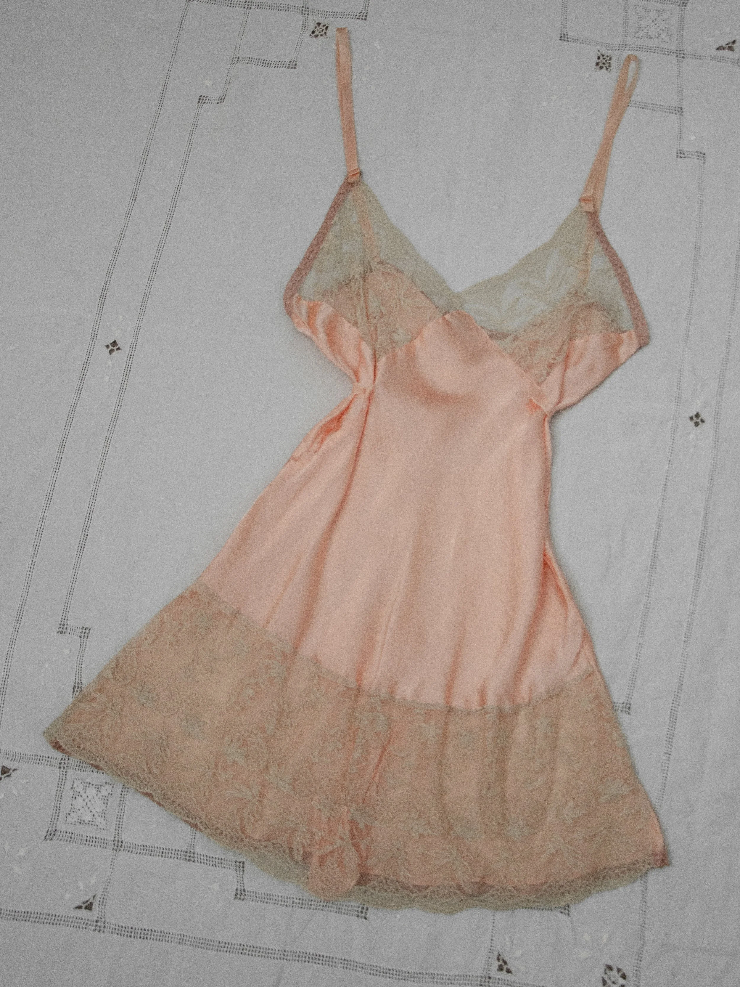 1930s blush pink silk longline teddy laid flat on white linen, full front view with lace trims.