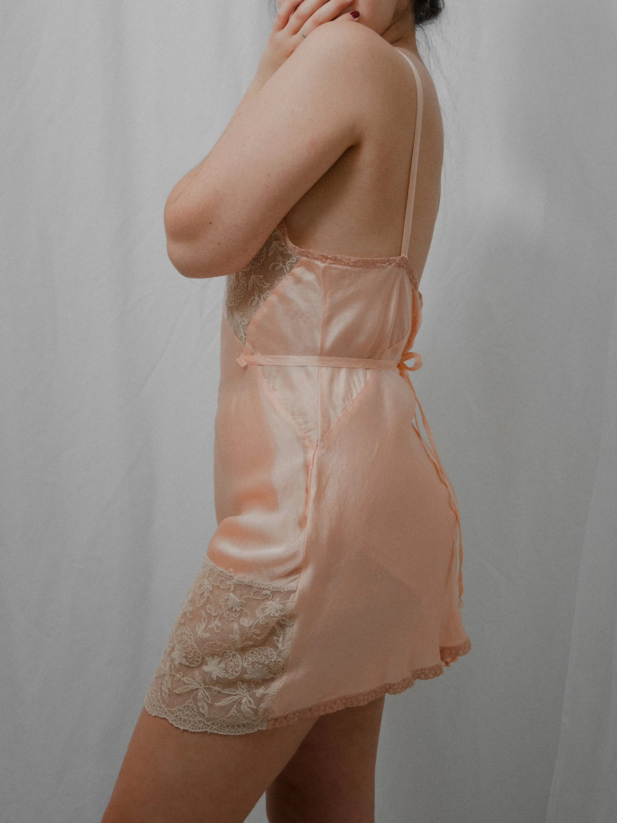 Side view of the 1930s blush silk teddy on a model, showing the ribbon straps and lace hem.