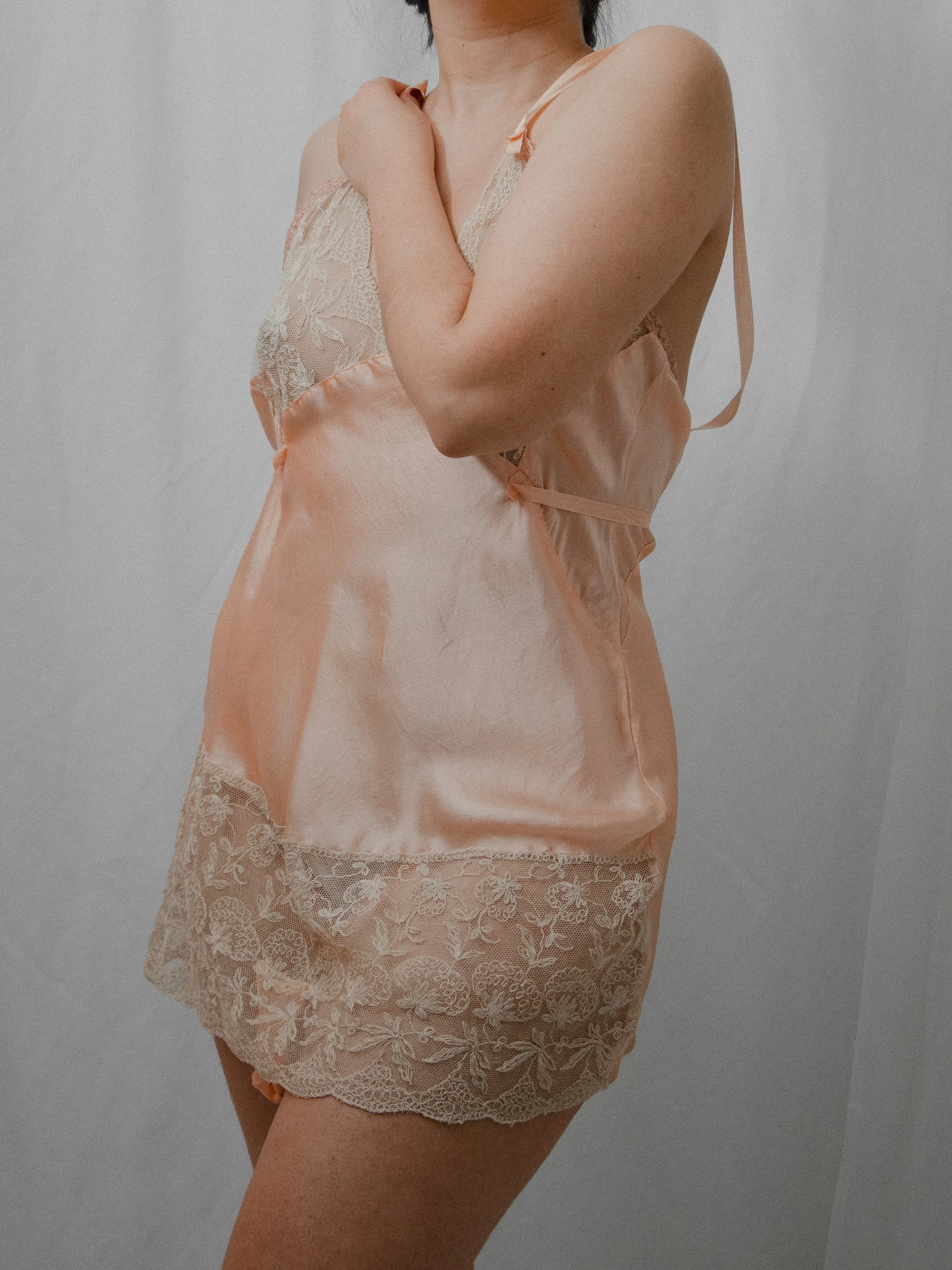 1930s blush pink silk teddy worn on a model, three-quarter view with lace bodice and hem.