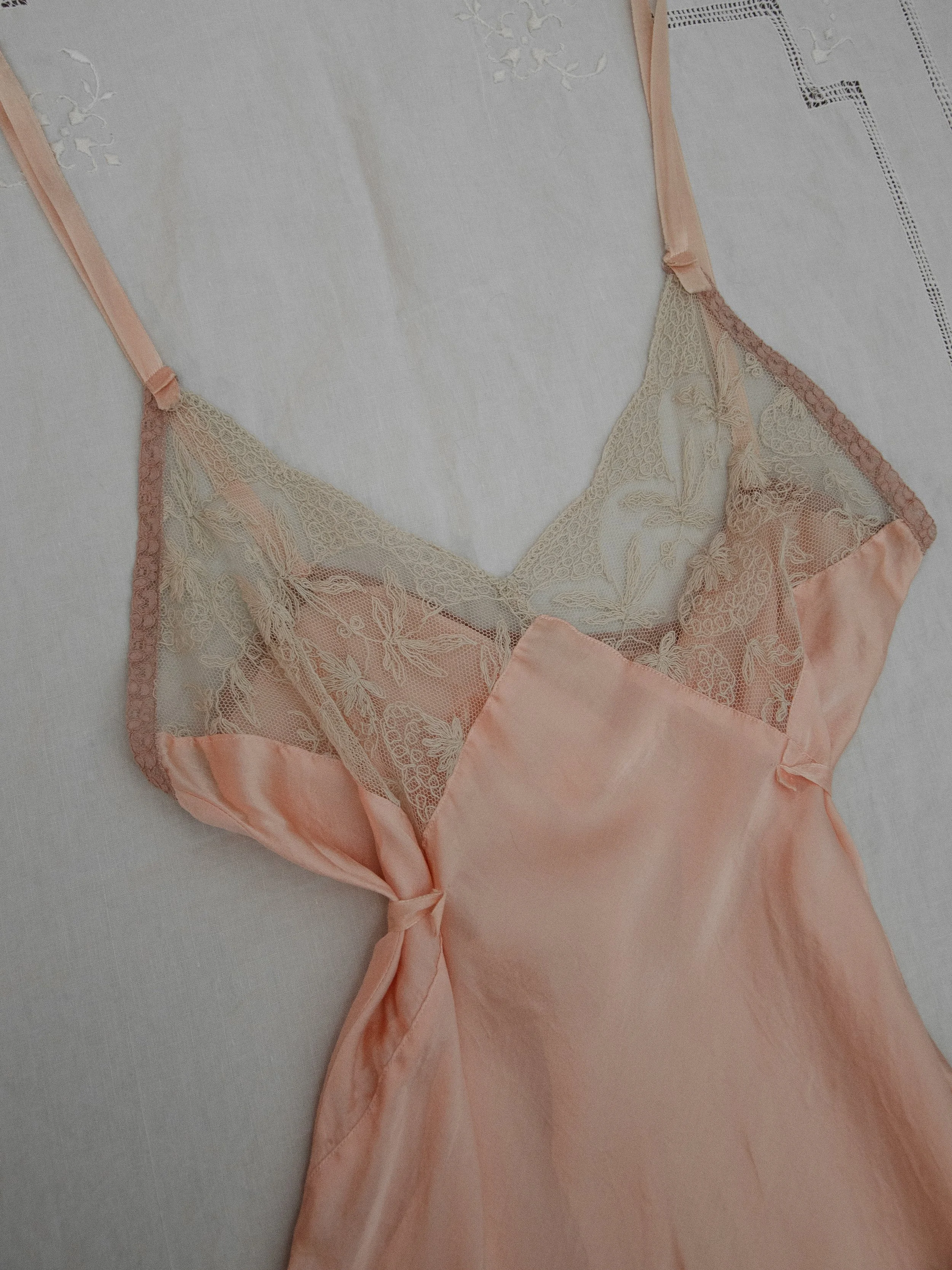 Close-up of the 1930s pink silk teddy laid flat, showing the ecru lace bodice and waist tie.