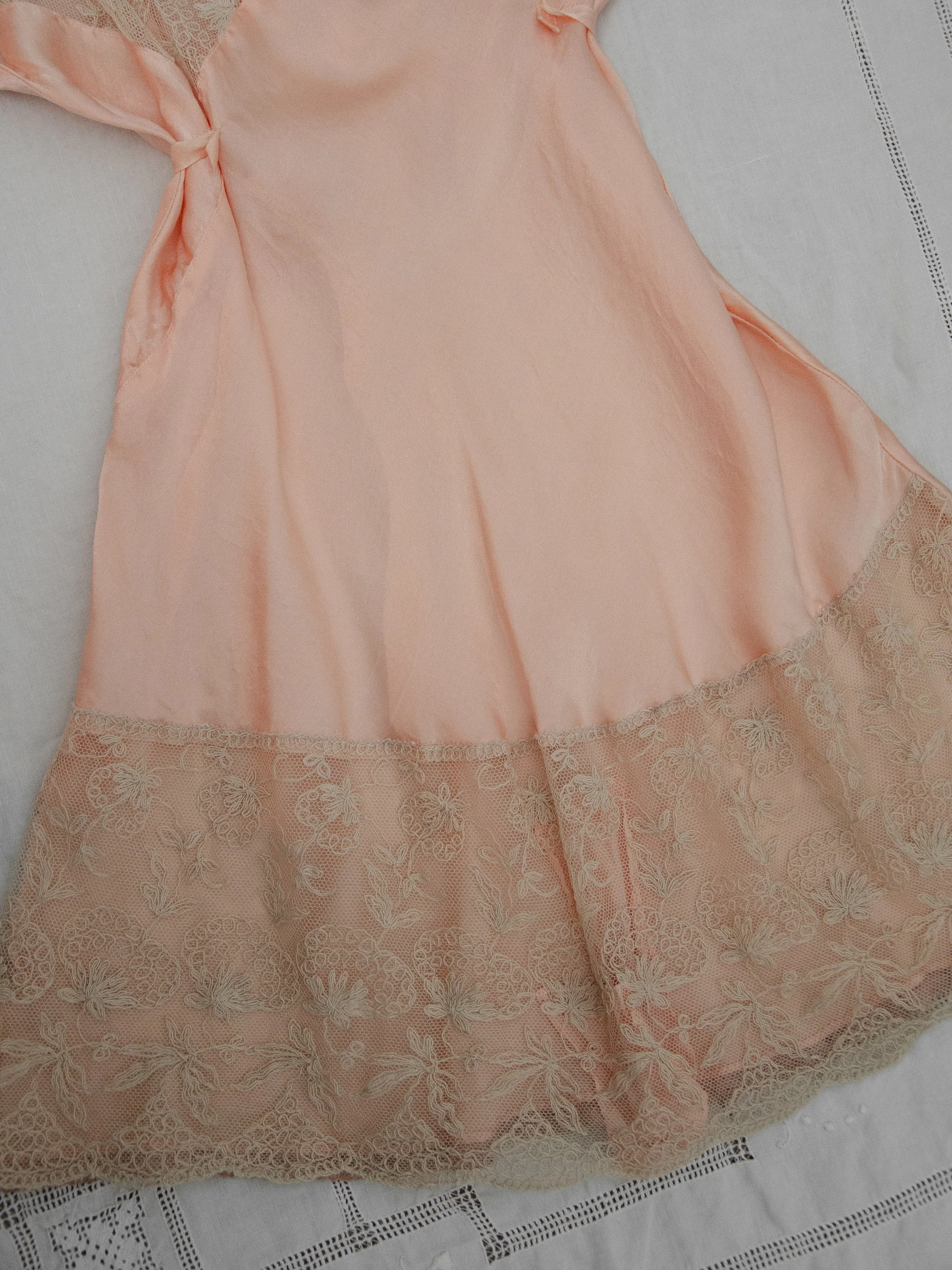 Detail of the 1930s blush silk teddy laid flat, showing the deep ecru lace border at the hem.