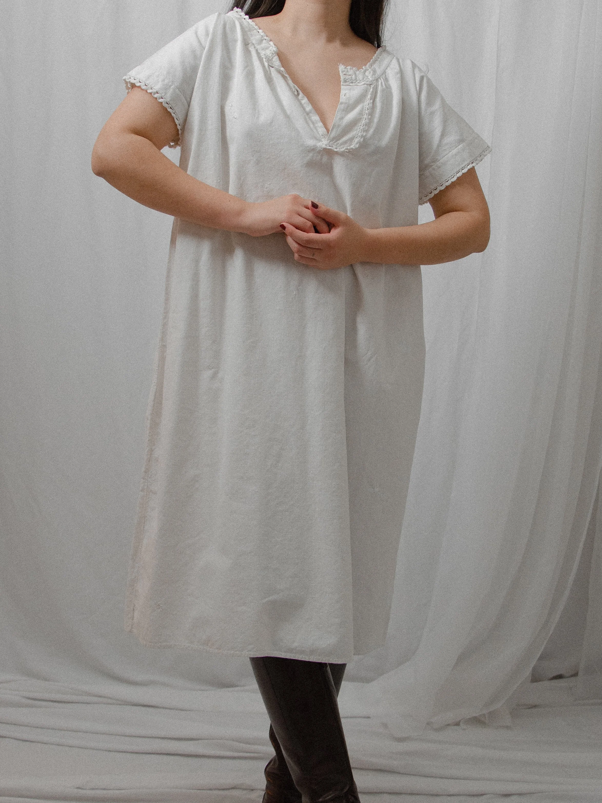1860s Victorian white cotton smock dress on a model with hands clasped, showing its loose knee-length shape.